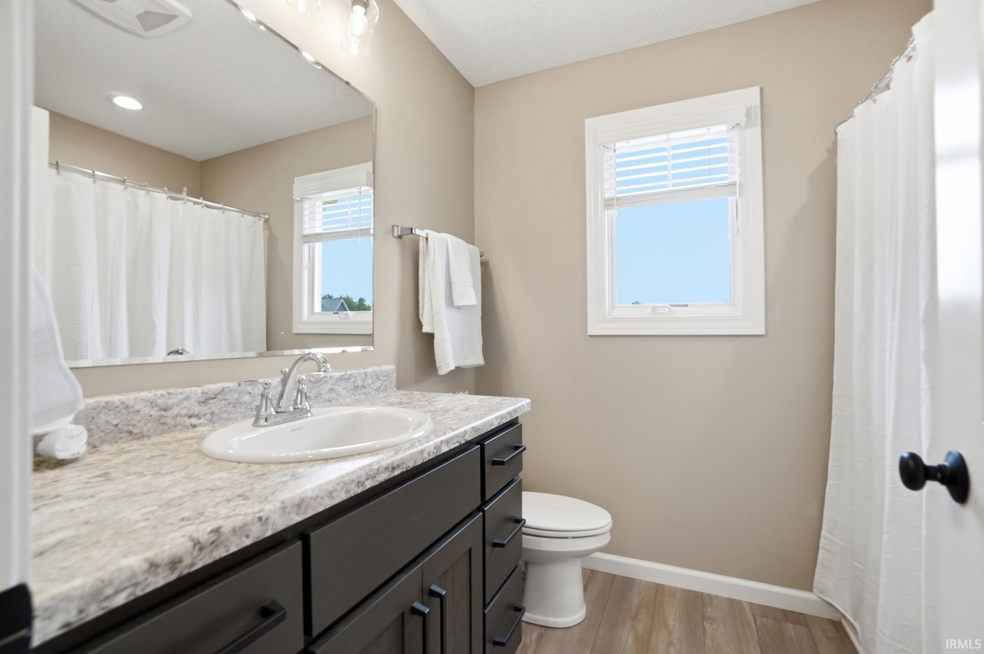 Bathroom featuring a dark wood vanity with a light-toned countertop, a built-in sink with chrome fixtures, a large wall mirror, and wood-finish flooring