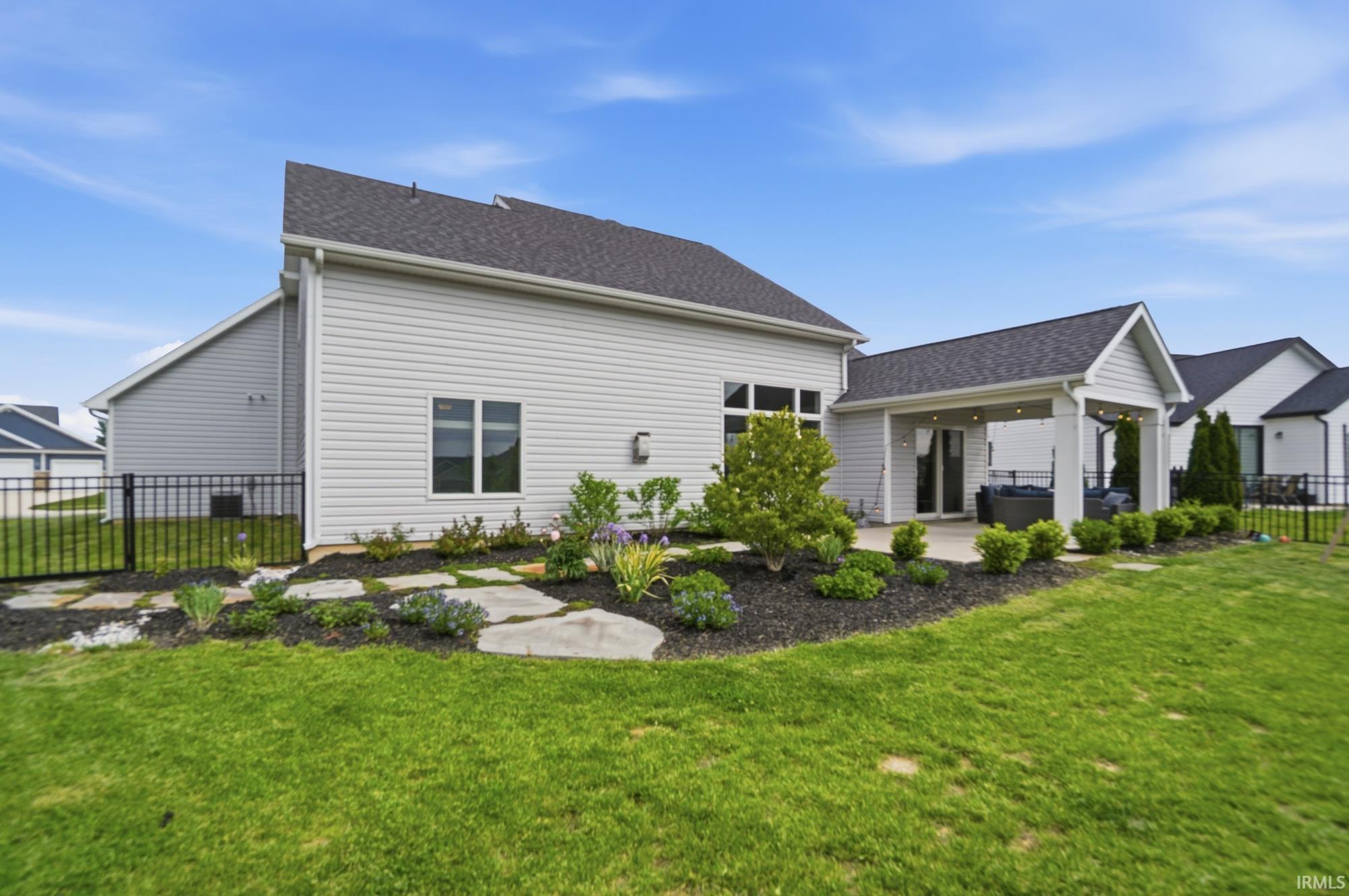 Rear exterior featuring a covered patio, expansive lawn, and landscaping with stepping stones