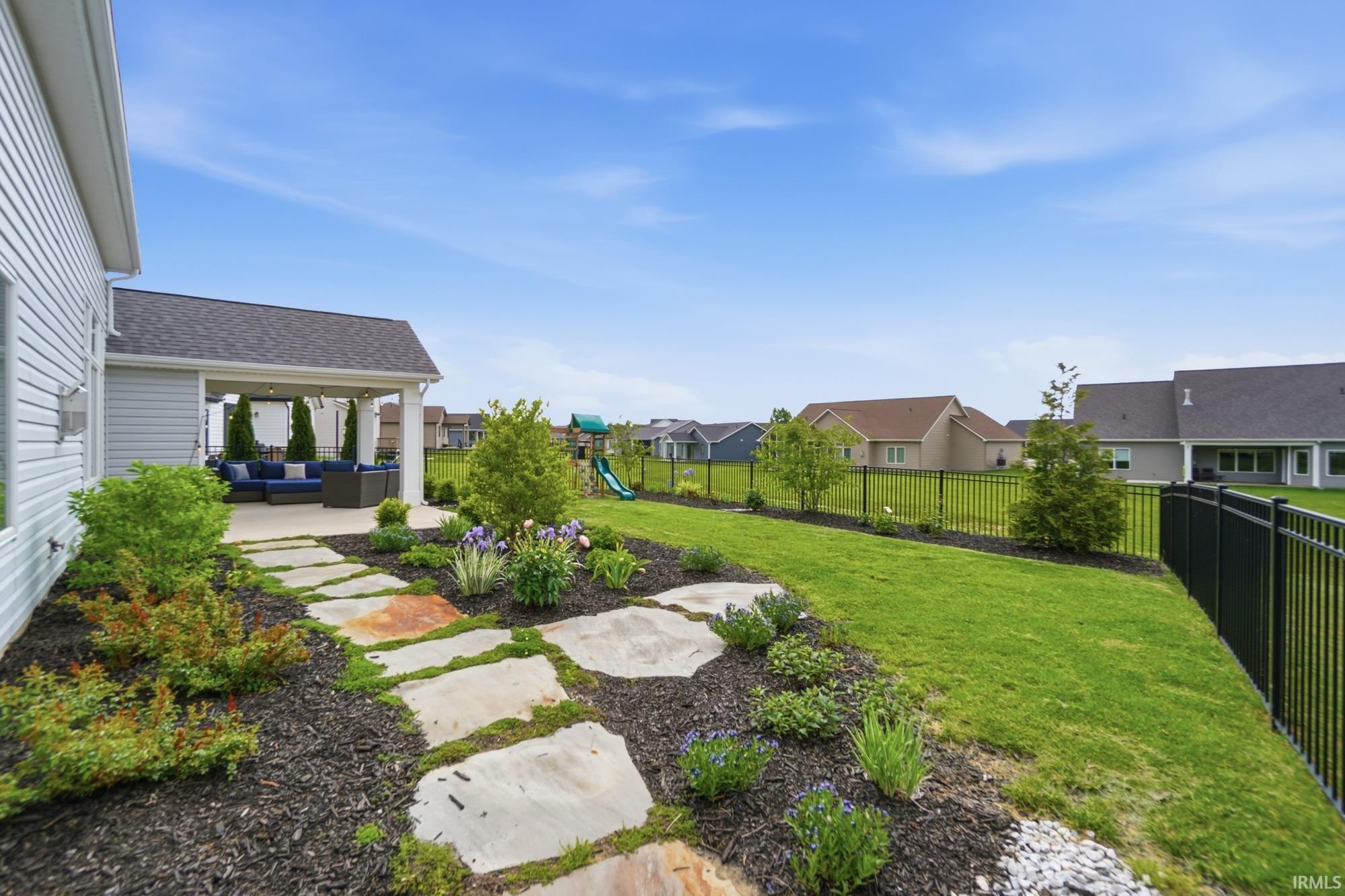 Manicured backyard featuring a covered patio, extensive lawn, and a stone-paver pathway