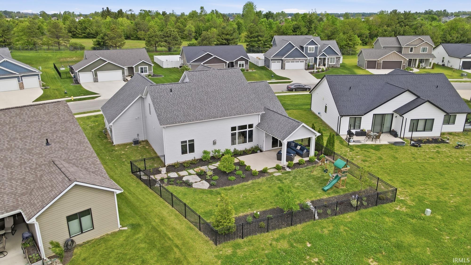 Spacious backyard featuring a covered patio, additional open patio space, mature landscaping, and a black metal fence