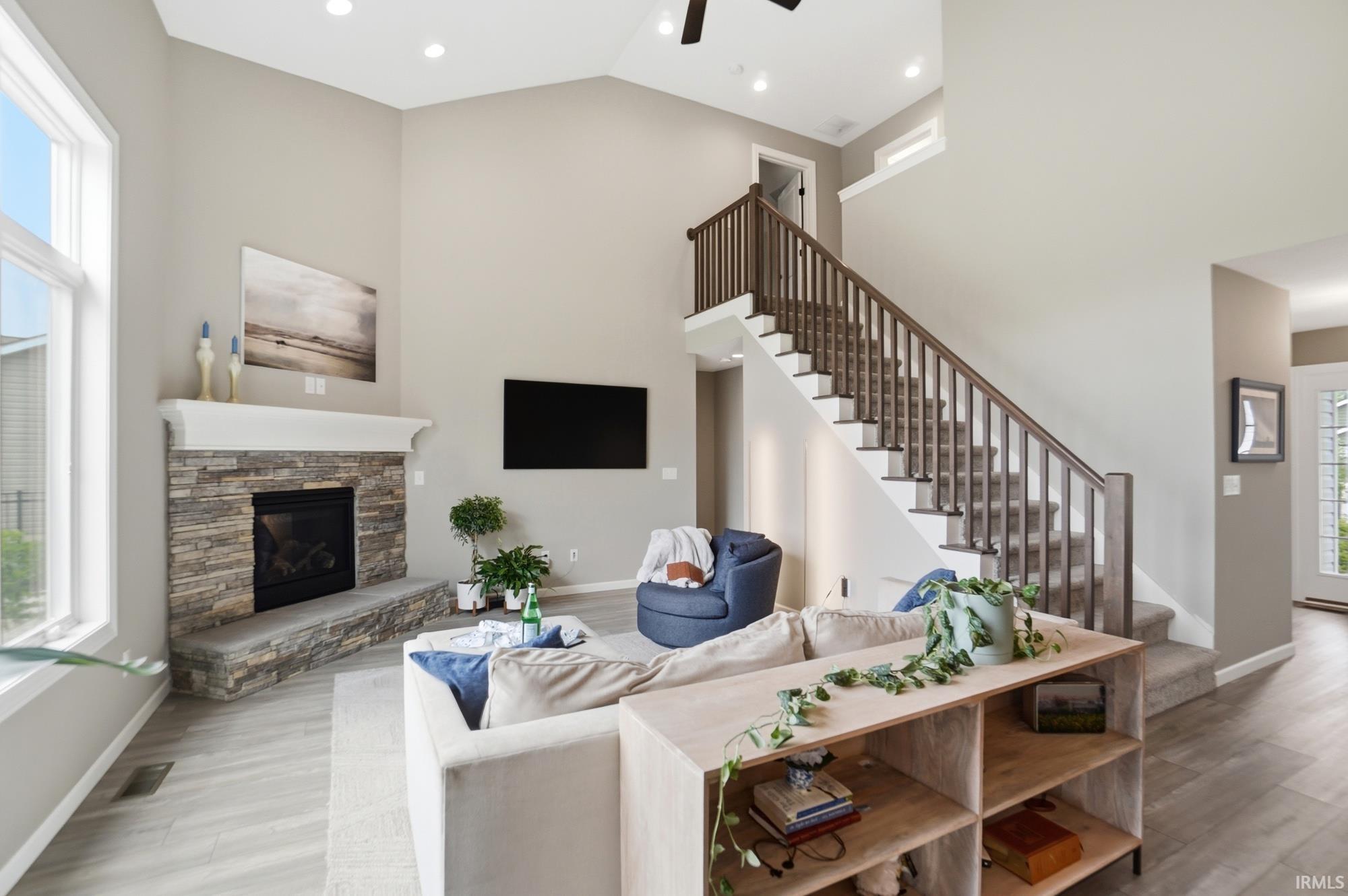 Spacious living area featuring vaulted ceilings, large windows, a stacked stone fireplace with a substantial hearth and mantel, and wood-finish flooring