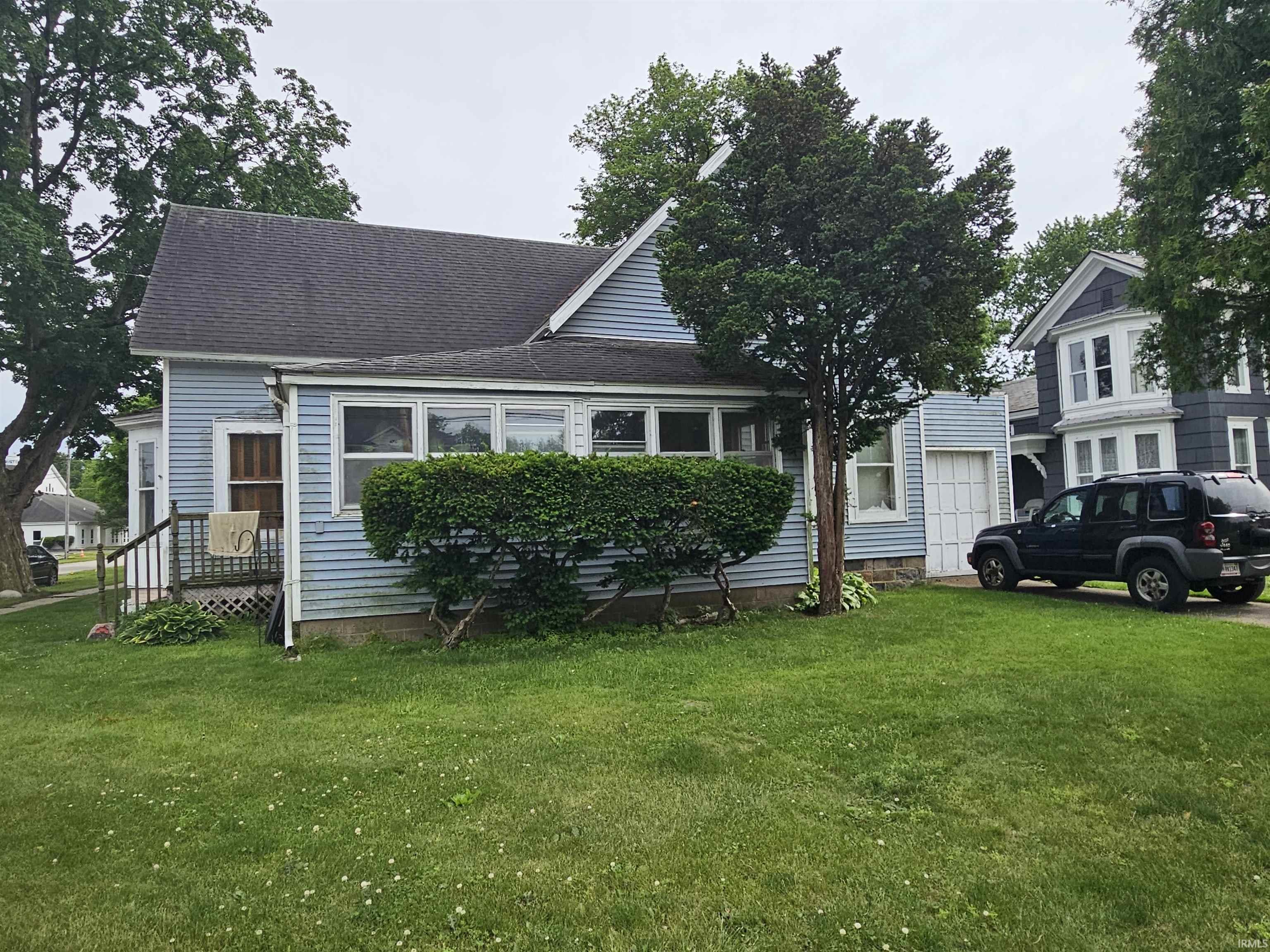 Light blue horizontal siding exterior with a dark shingle roof and a covered front porch featuring lattice skirting