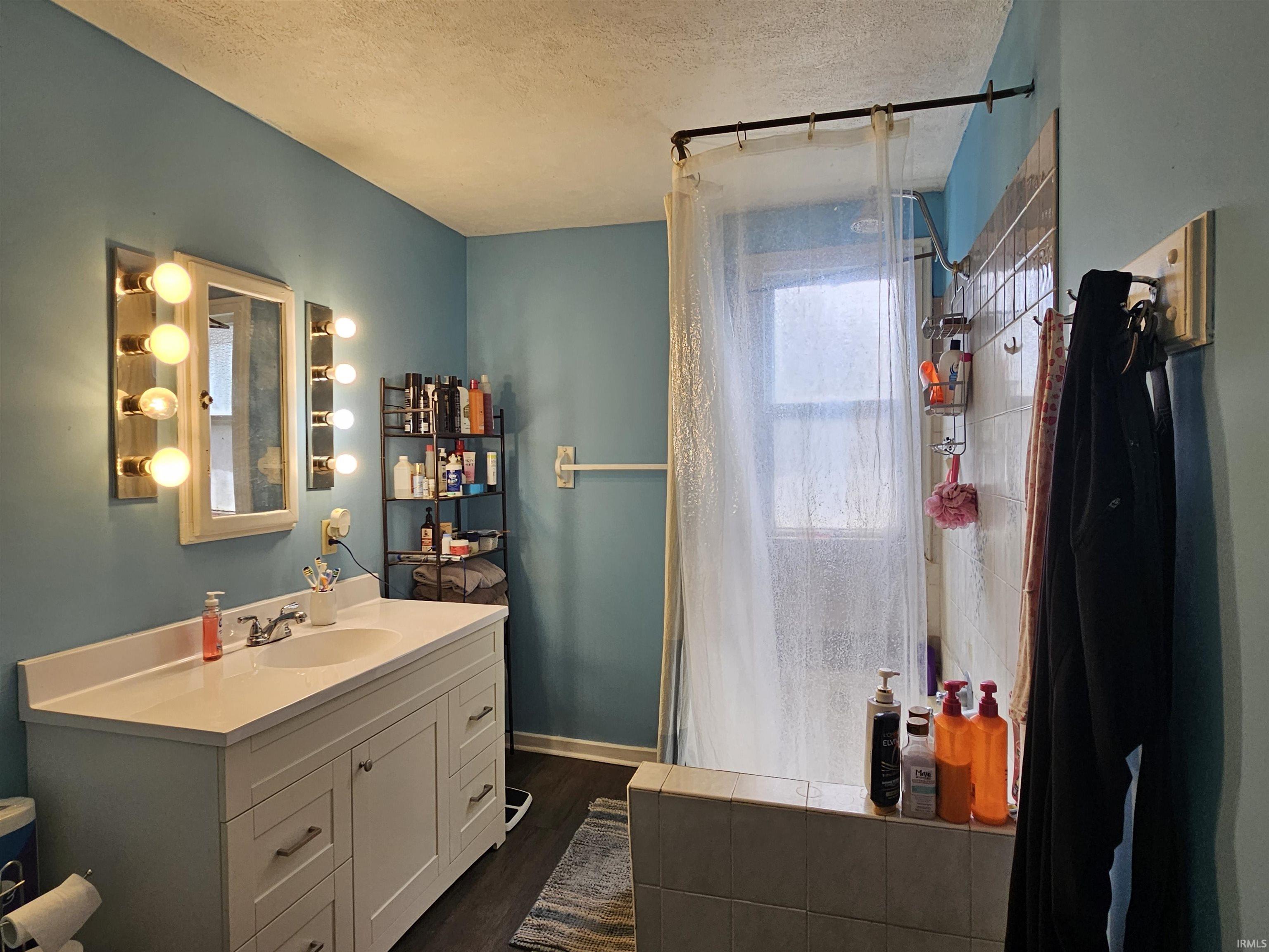 Bathroom featuring a white vanity with an integrated sink, dual vanity light fixtures, a framed mirror, and a shower/tub combination with a window