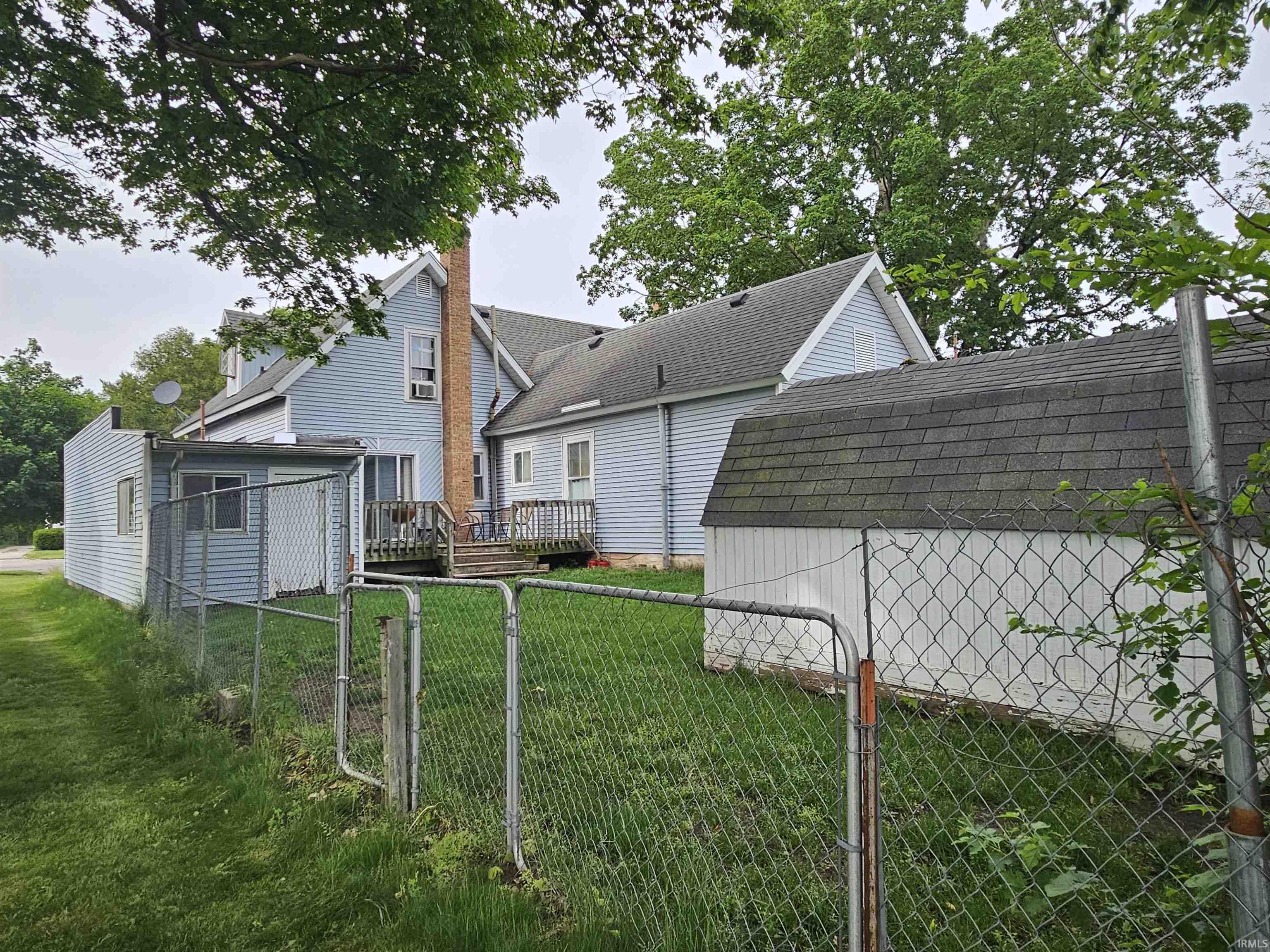 Rear exterior of a light blue siding home featuring a wood deck, a brick chimney, and an attached enclosed porch