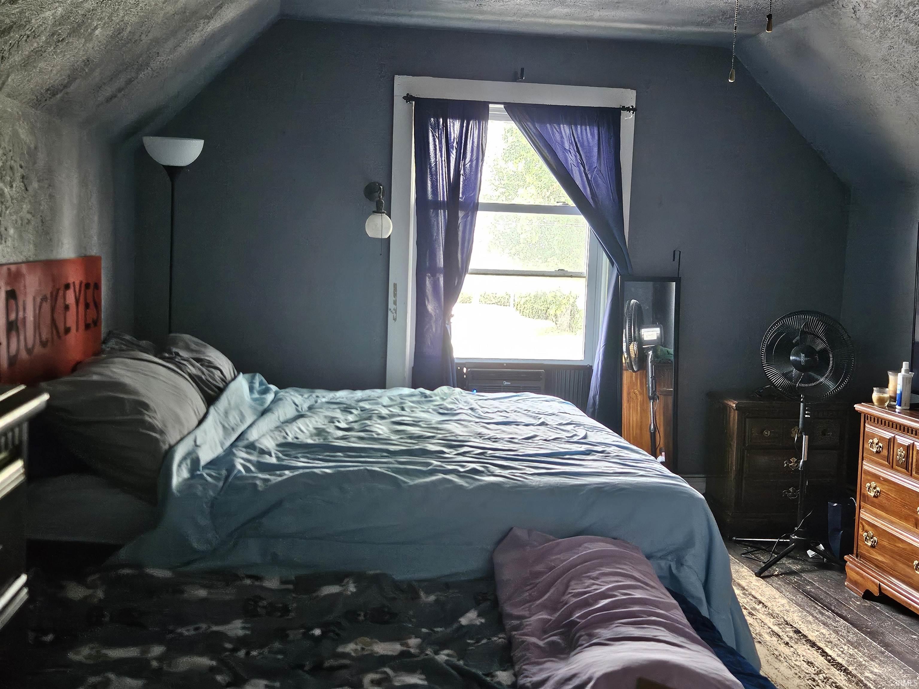 Attic space featuring sloped ceilings, a single window with white trim, and dark-stained wood-finish flooring