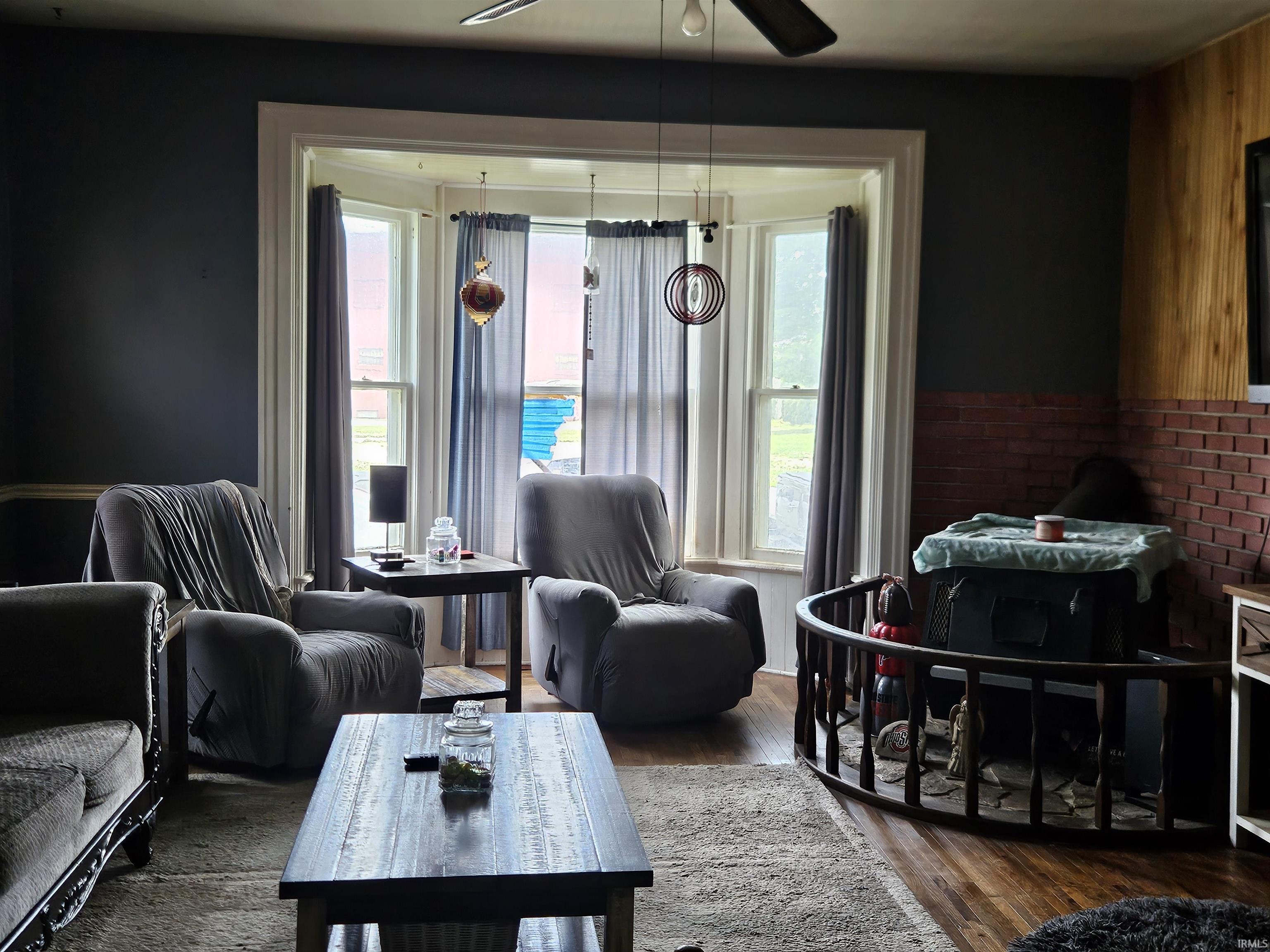 Living space featuring a bay window, wood-finish flooring, dark wall paint, and a textured accent wall with a brick-like pattern