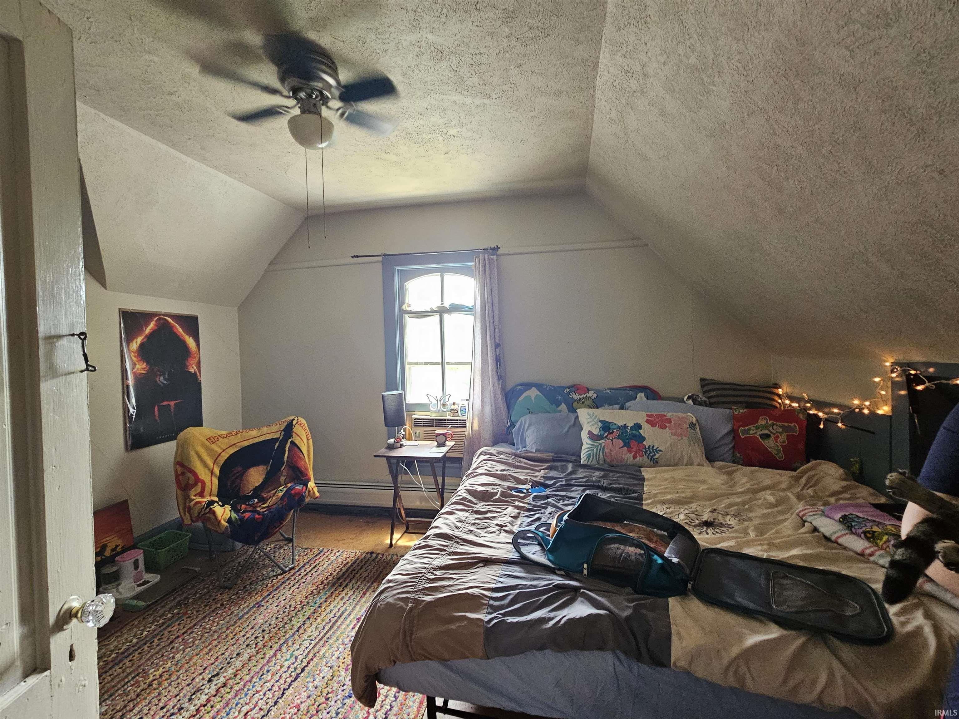 Attic room featuring sloped ceilings, a ceiling fan with light fixture, and a window with a rounded top sash