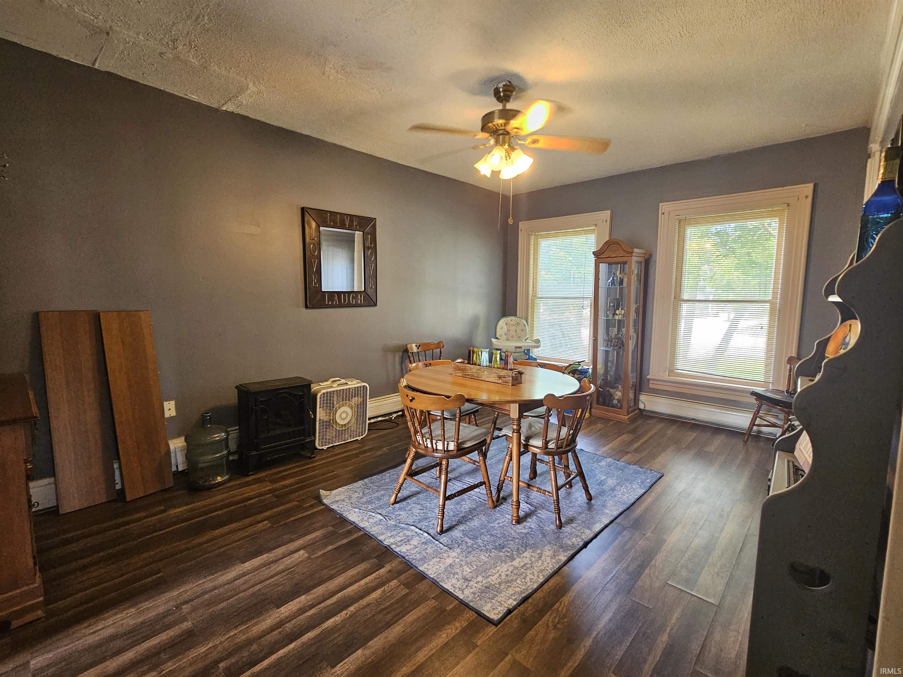 Spacious room featuring wood-finish flooring, two large windows with white trim, and a ceiling fan with integrated lighting