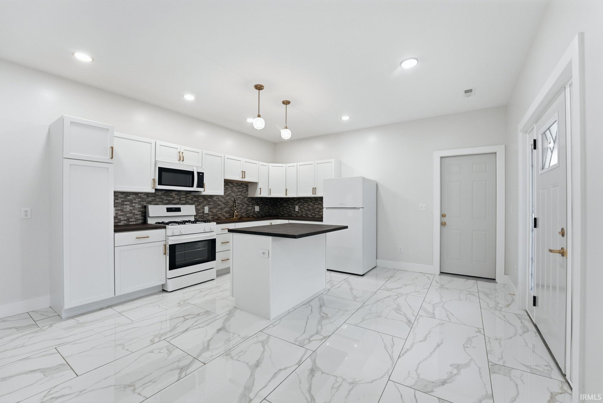 Kitchen featuring white cabinetry, dark countertops, a dark mosaic tile backsplash, and white appliances