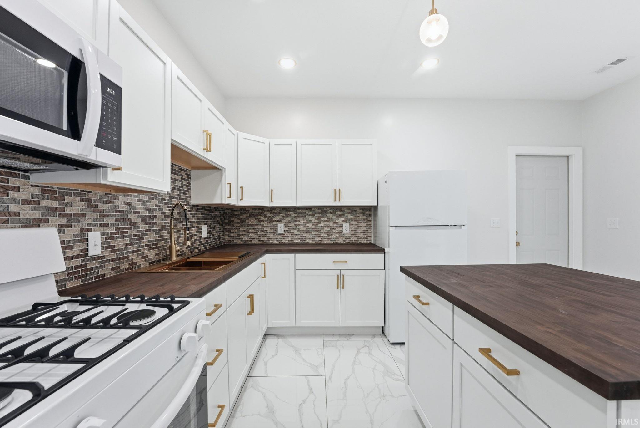 Contemporary kitchen featuring white cabinetry, wood-finish countertops, a mosaic tile backsplash, and white tile flooring