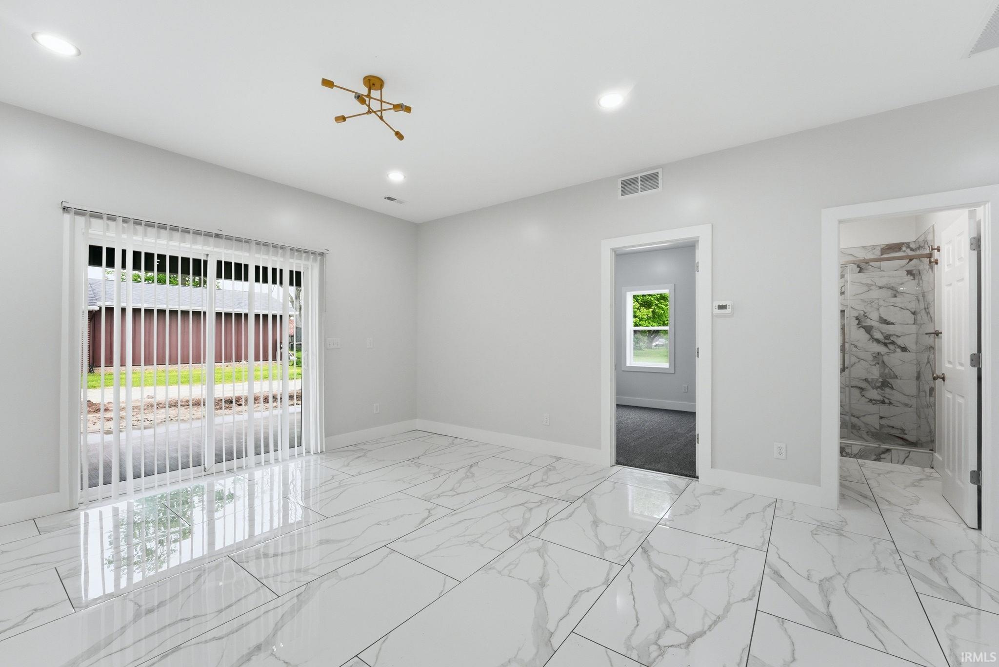 Spacious room featuring large format marble-look tile flooring, white vertical blinds on a sliding glass door, and a contemporary gold-finish chandelier