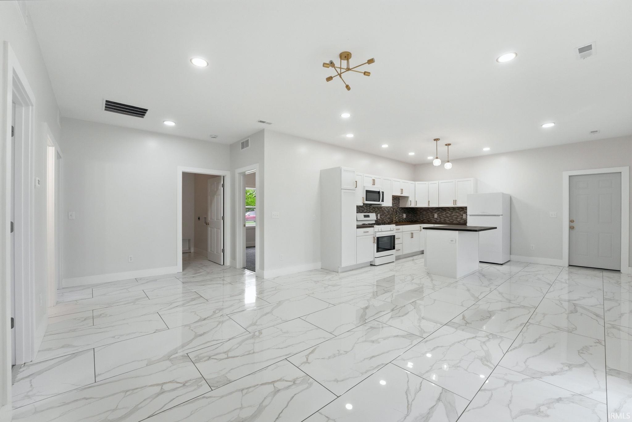 Open-concept living space with large format white tile flooring, recessed lighting, a modern sputnik chandelier, white kitchen cabinetry with dark countertops, and a central kitchen island
