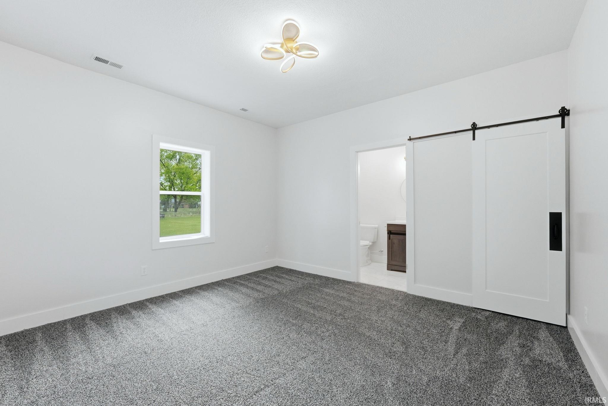 Carpeted room featuring a barn door entry, a single window, and a contemporary ceiling light fixture