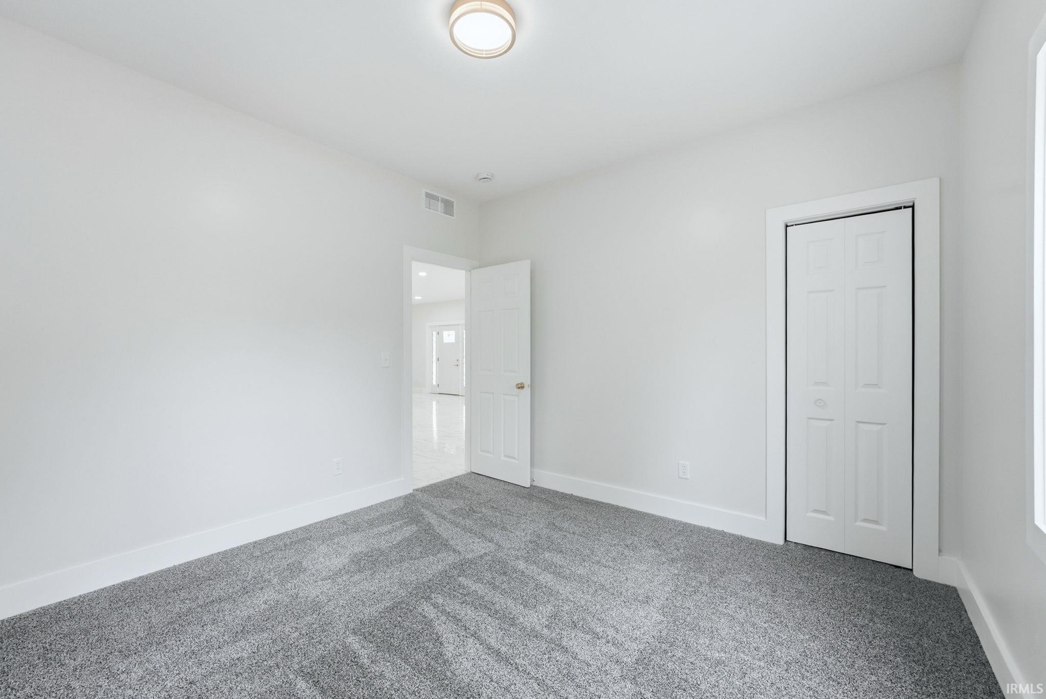 Room featuring light gray patterned carpet, white walls, white trim, and a white bi-fold closet door