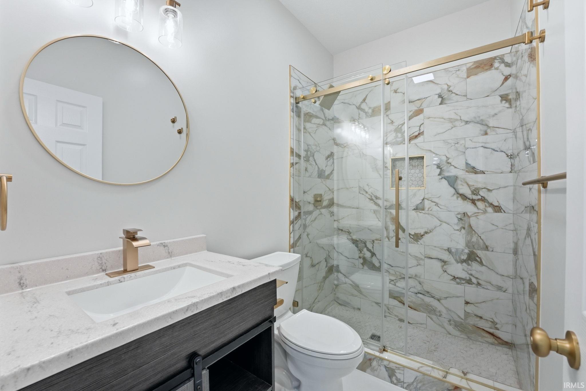 Modern bathroom featuring a vanity with a white countertop and rectangular undermount sink, brushed gold fixtures, and a shower with sliding glass doors and marble-patterned tile
