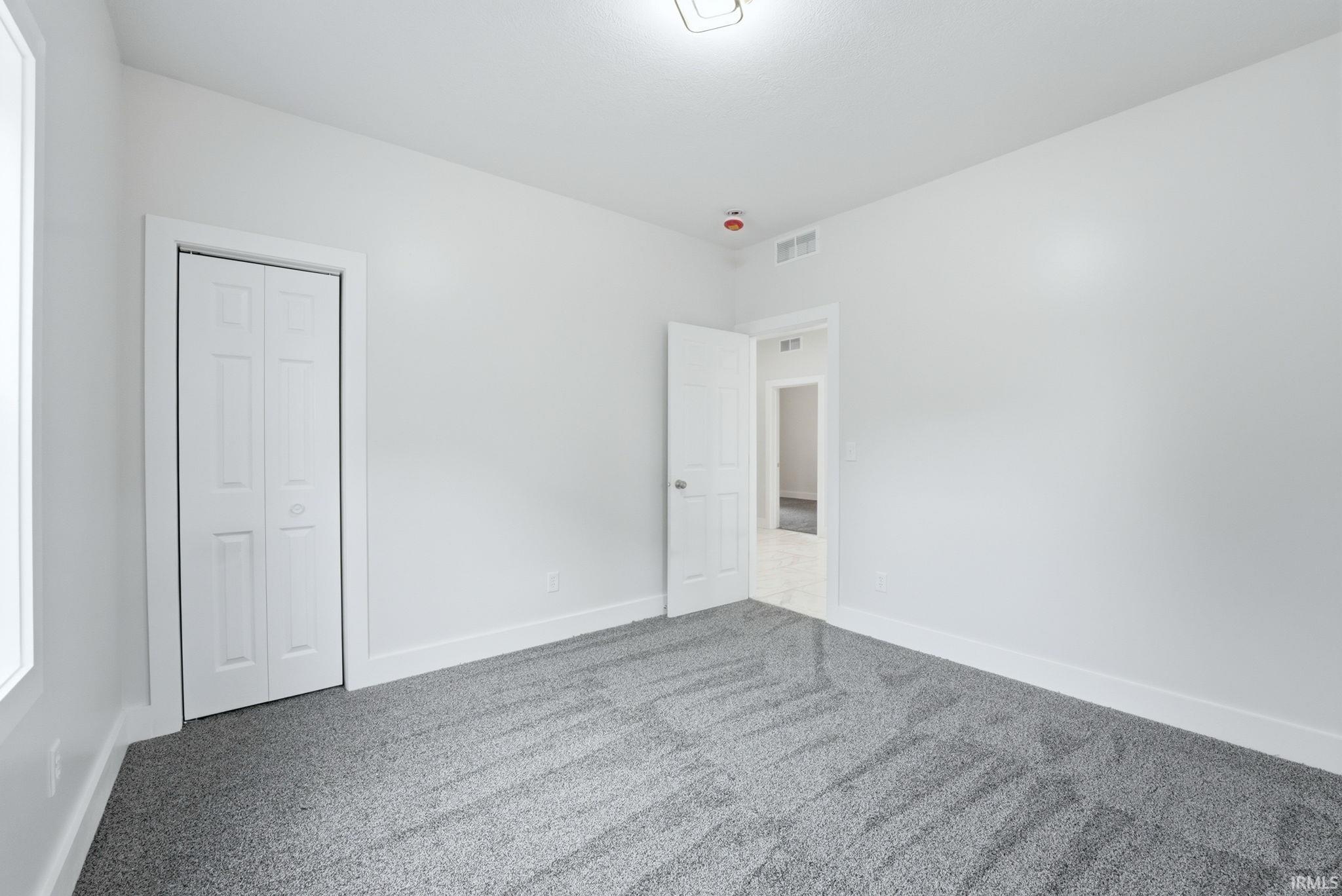 Room featuring light gray patterned carpeting, white walls, white baseboards, and a white bi-fold closet door