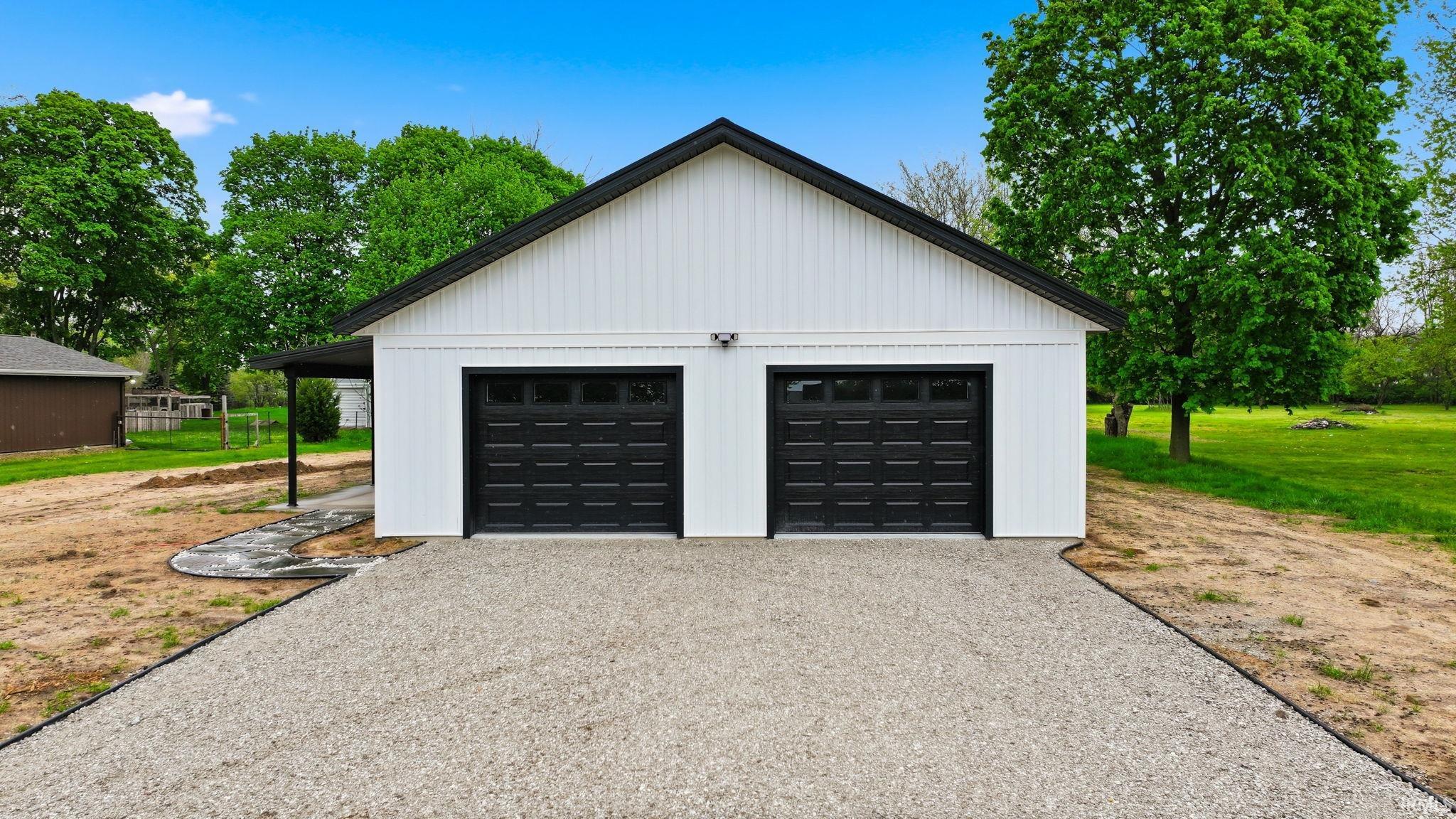 New construction two-car garage featuring white vertical siding, black trim, and black garage doors