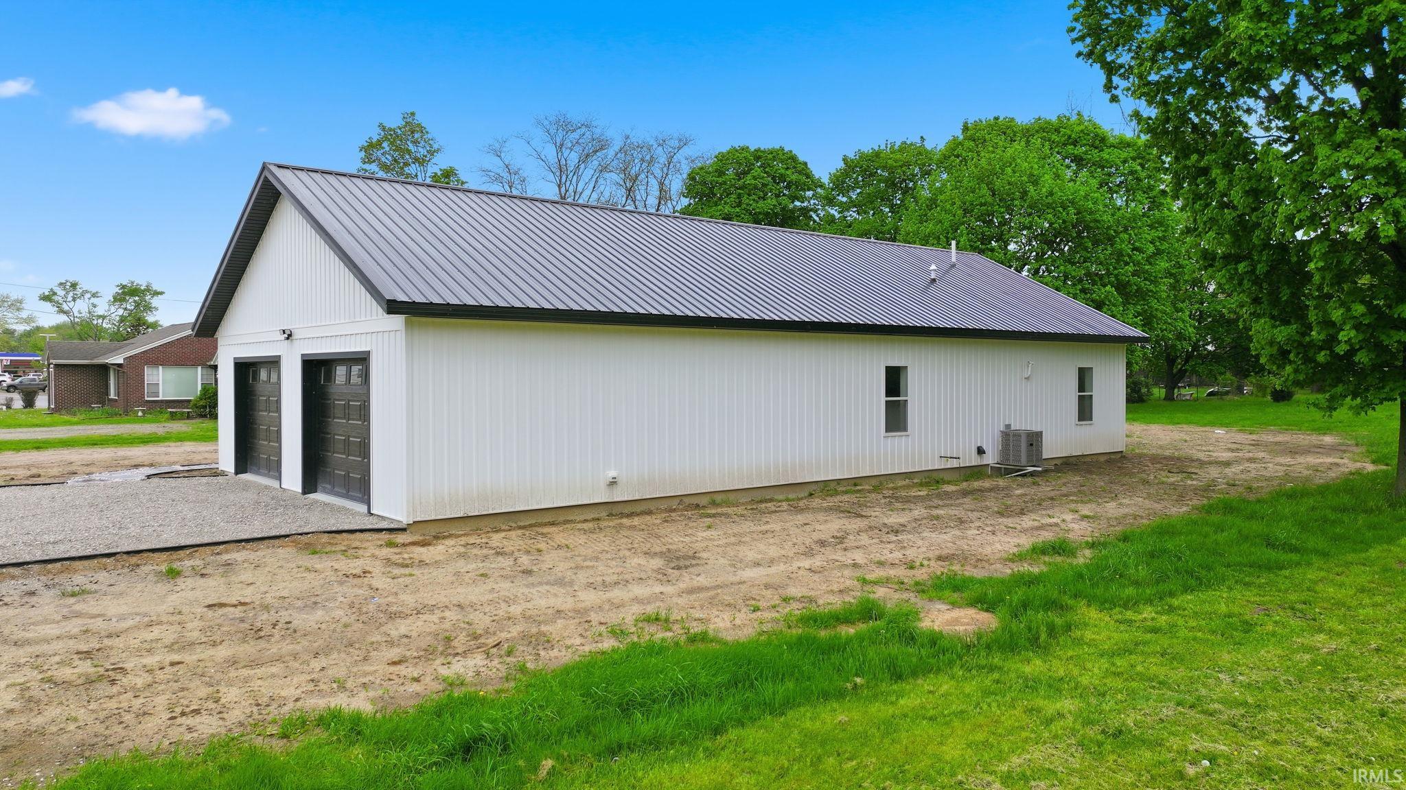 Detached structure featuring a dark gray metal roof, white vertical panel siding, and two black garage doors
