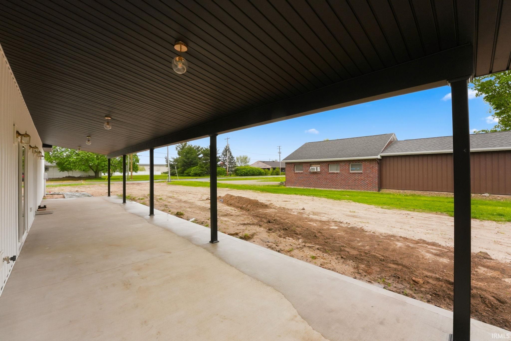 Expansive covered concrete patio featuring a dark wood-finish ceiling, multiple recessed light fixtures, and a series of black support columns