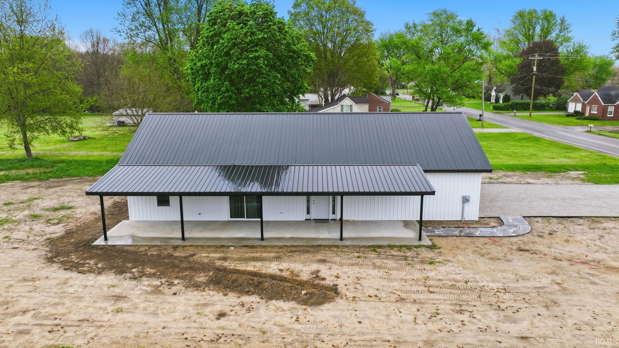 Modern farmhouse style property featuring a striking black metal roof, white siding, a covered concrete porch, and a gravel driveway
