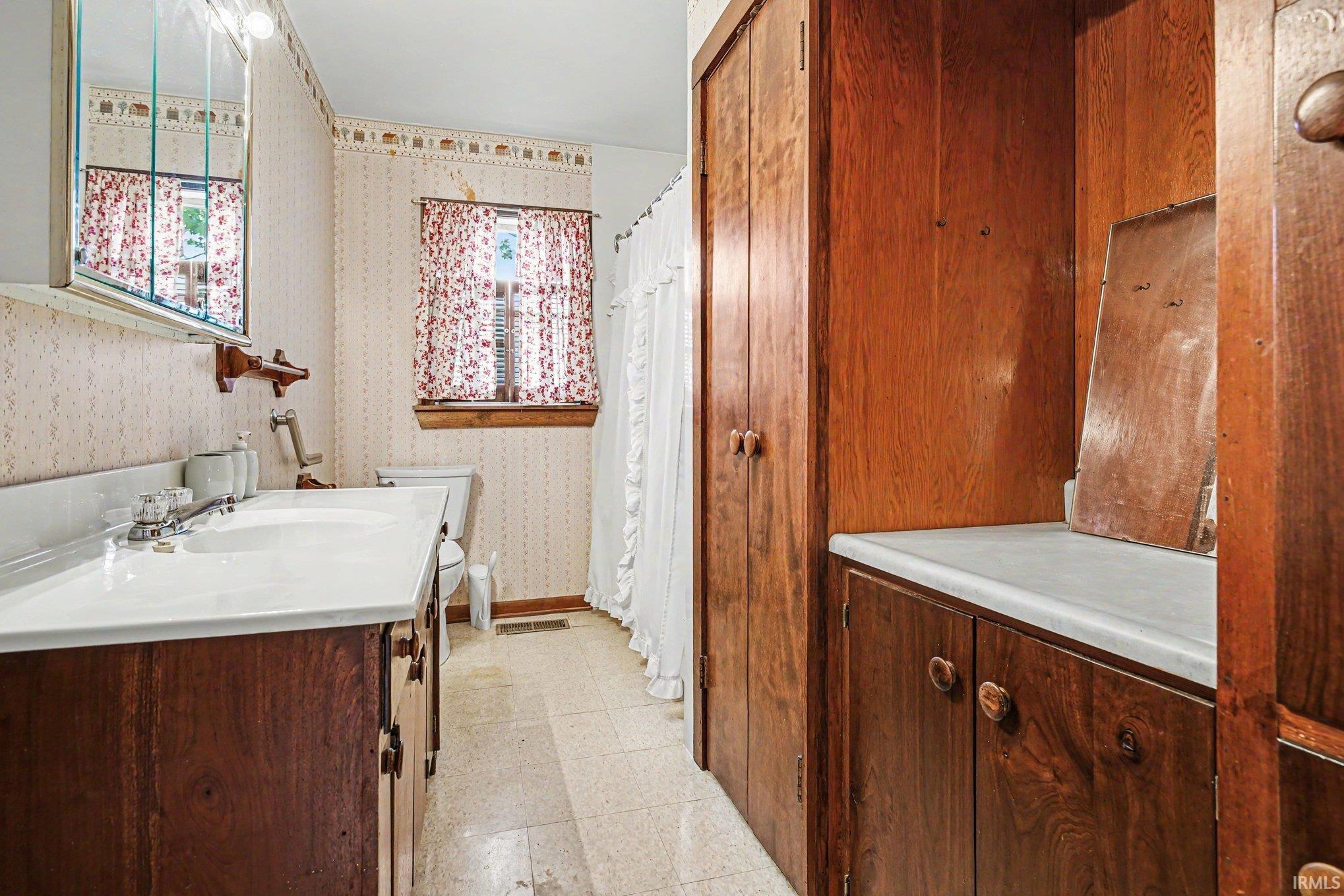 Bathroom featuring a double vanity with white basin sinks, a wall-mounted mirrored medicine cabinet, and a built-in storage cabinet with a white countertop