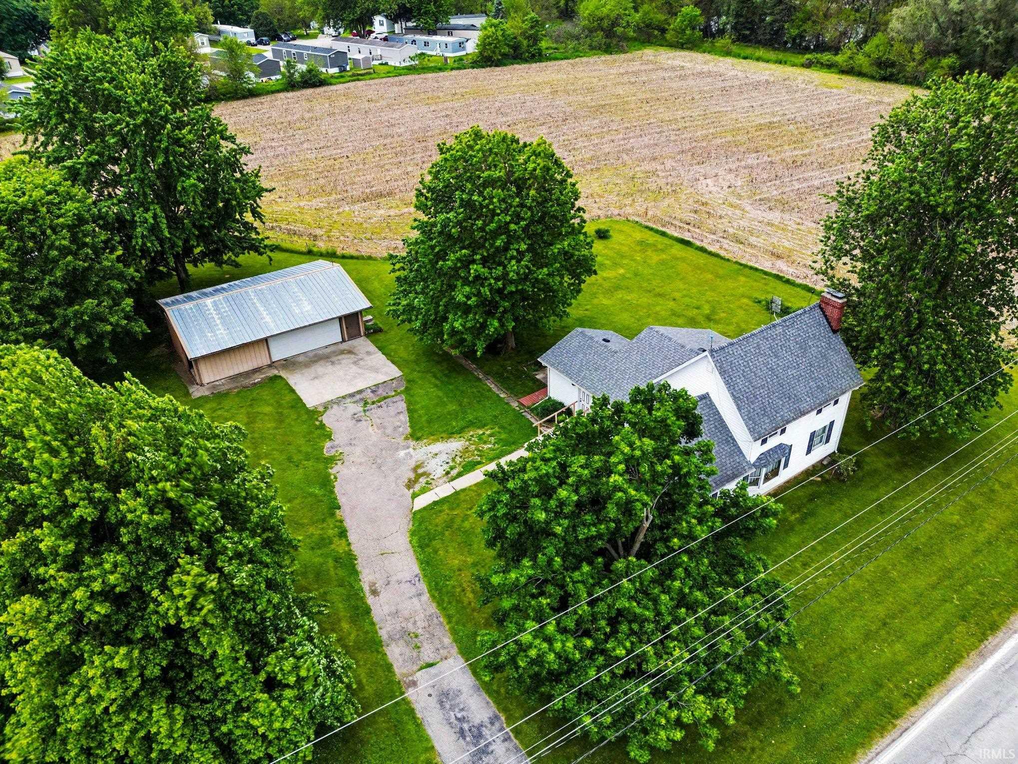 Aerial view of a residential property featuring a white two-story house with a grey shingle roof and green shutters
