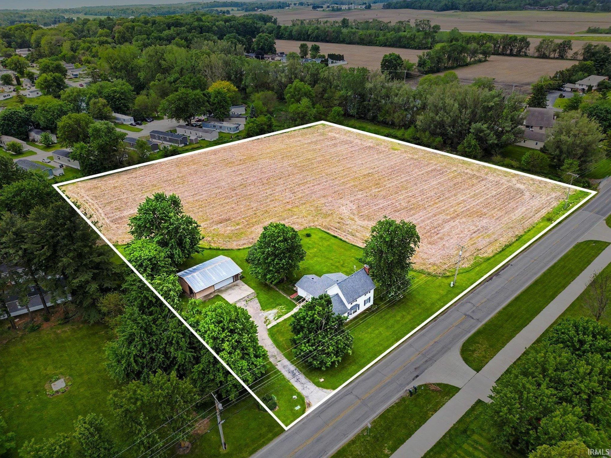 Expansive property featuring a two-story residence, separate outbuilding, paved driveway, mature trees, and a field