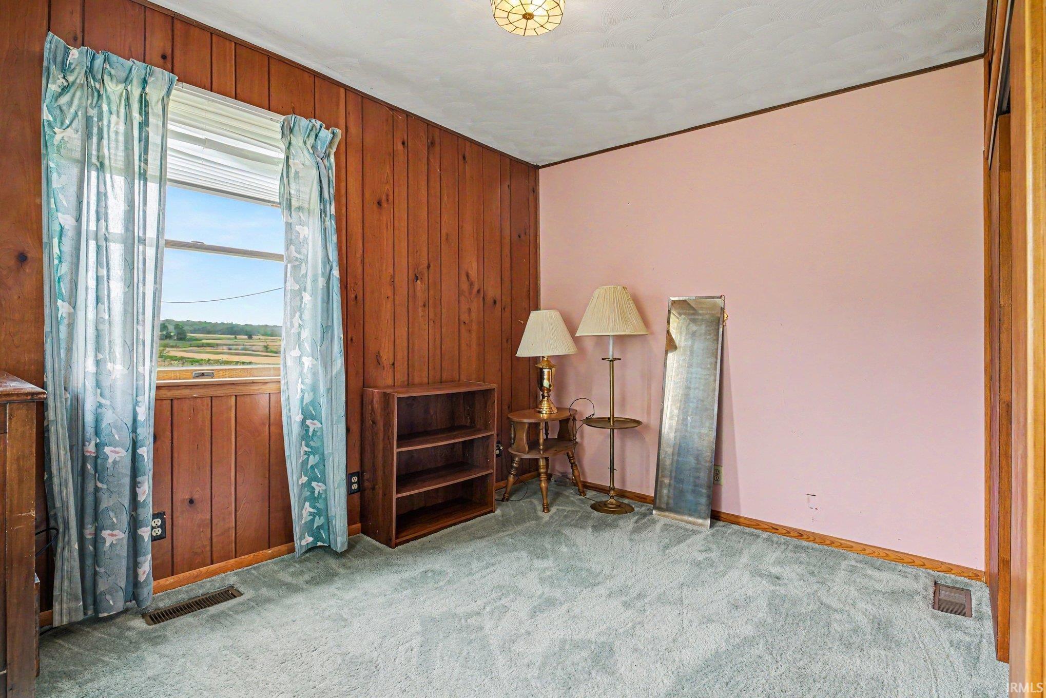 Room featuring wood-paneled walls, a painted accent wall, and a large window with horizontal blinds