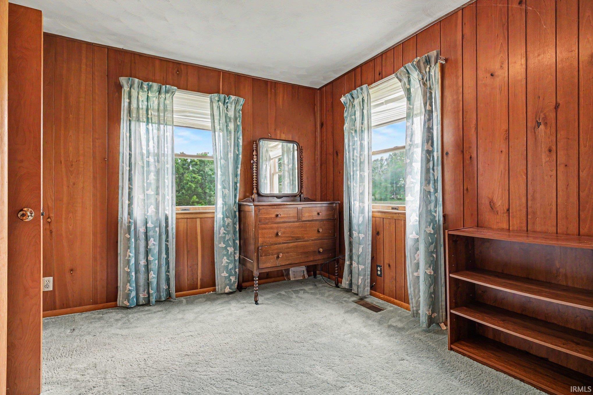 Interior room featuring wood paneling throughout, light blue carpeting, and two windows