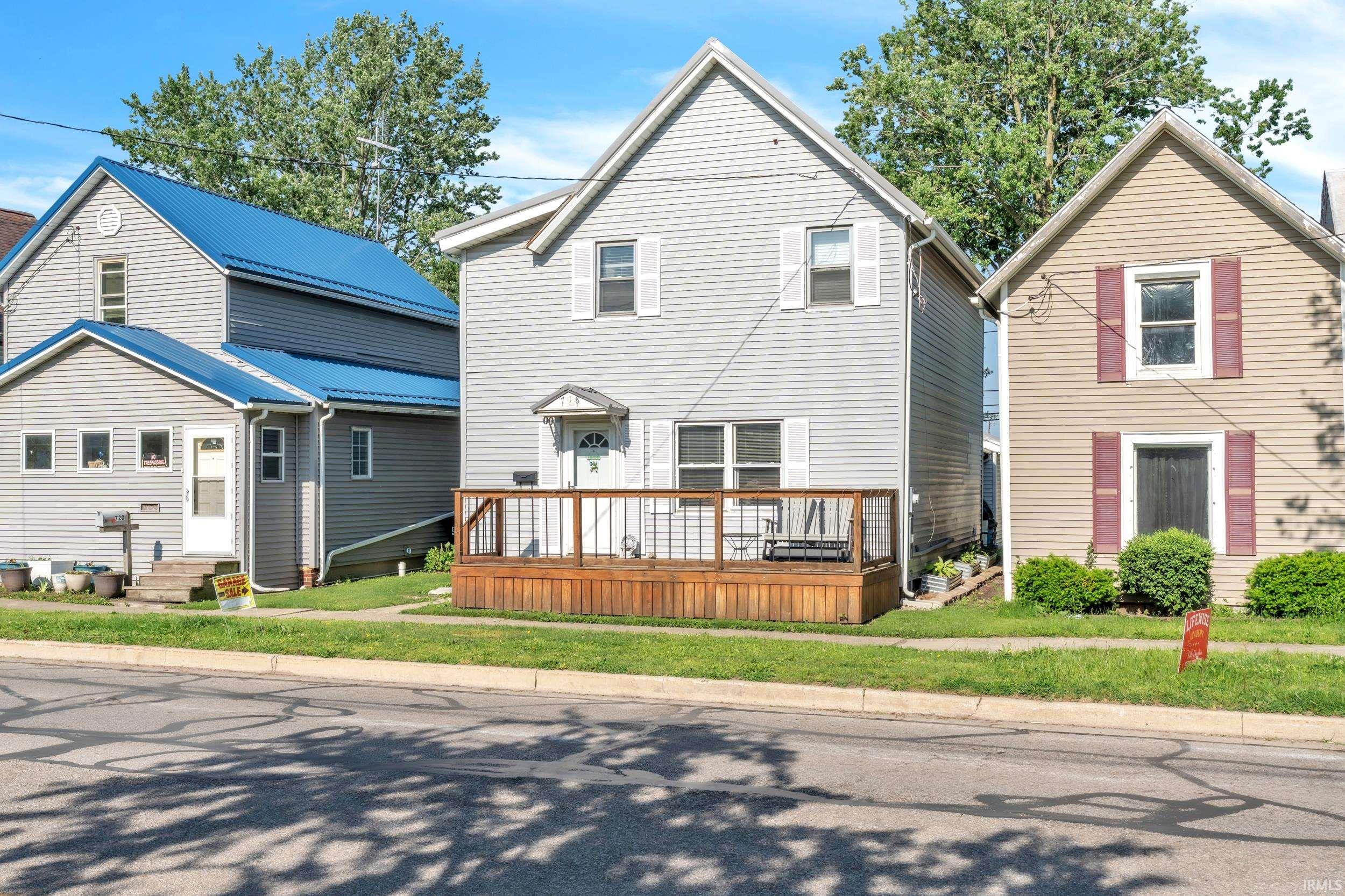 Light gray vinyl siding exterior featuring white window shutters, a front entry deck with a white railing, and a covered porch entry