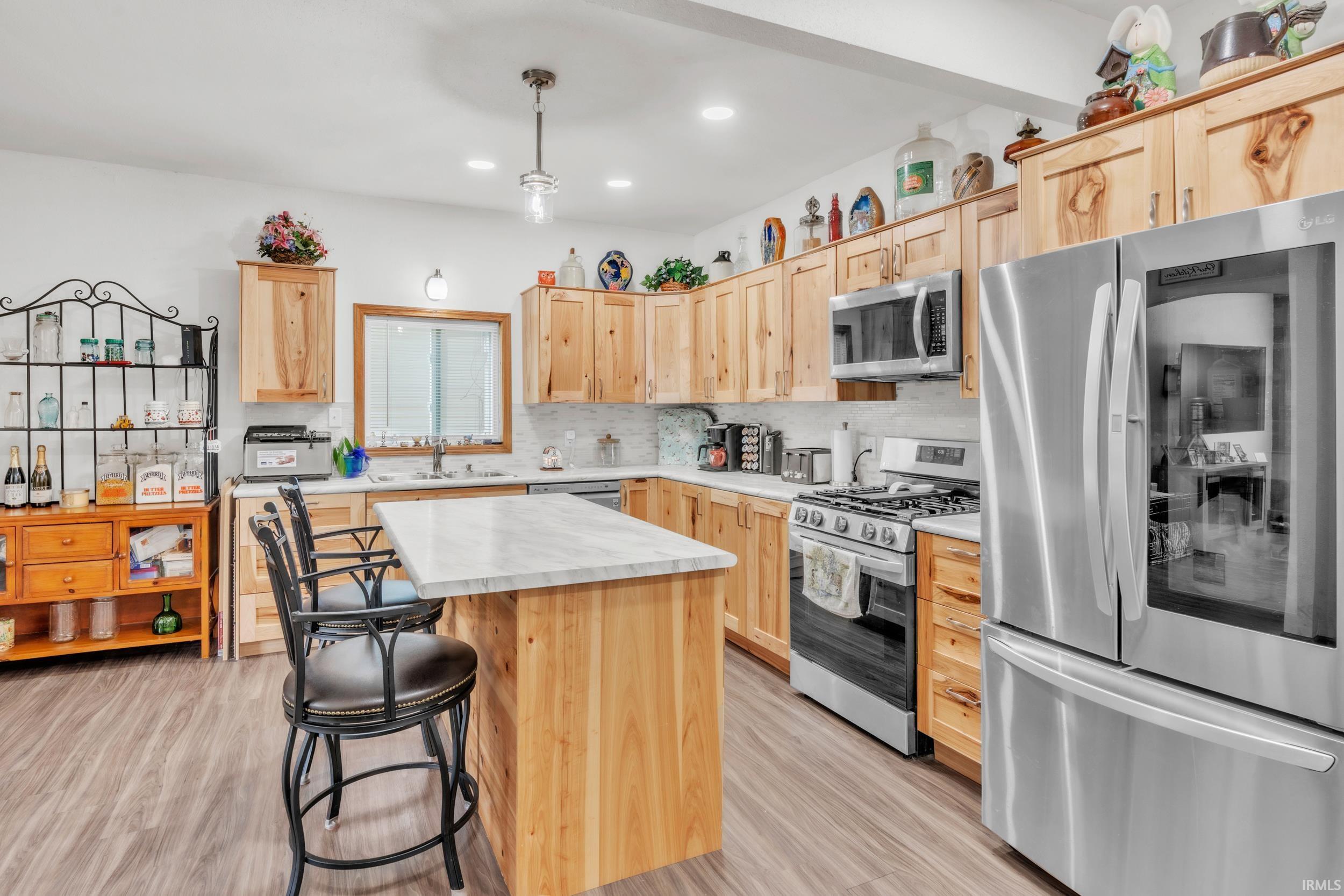 Kitchen featuring a central island with a light-toned countertop, wood-finish flooring, natural wood cabinetry, stainless steel appliances, and recessed lighting