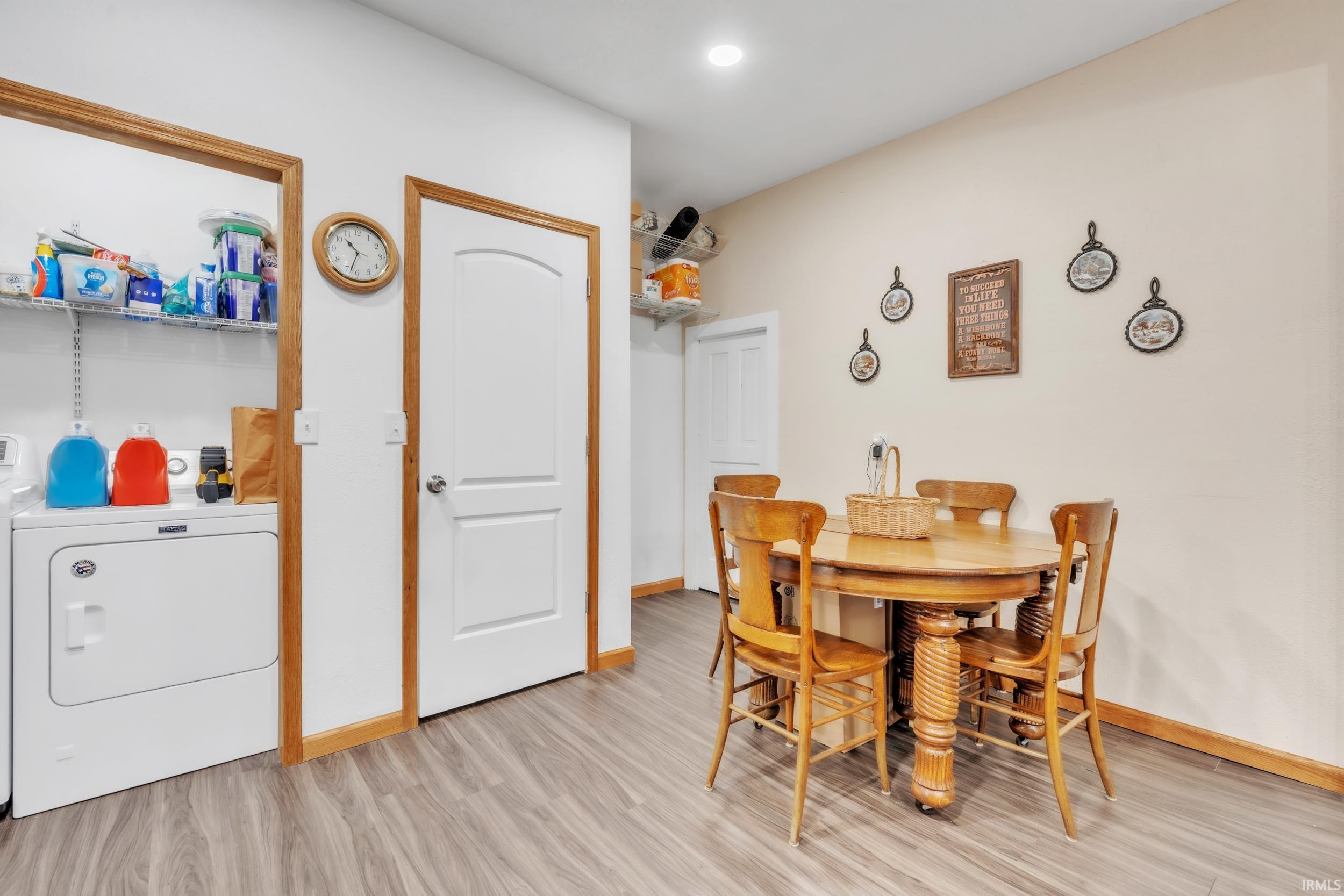 Utility area with laundry appliances and shelving, featuring wood-finish flooring and white interior doors with wood trim