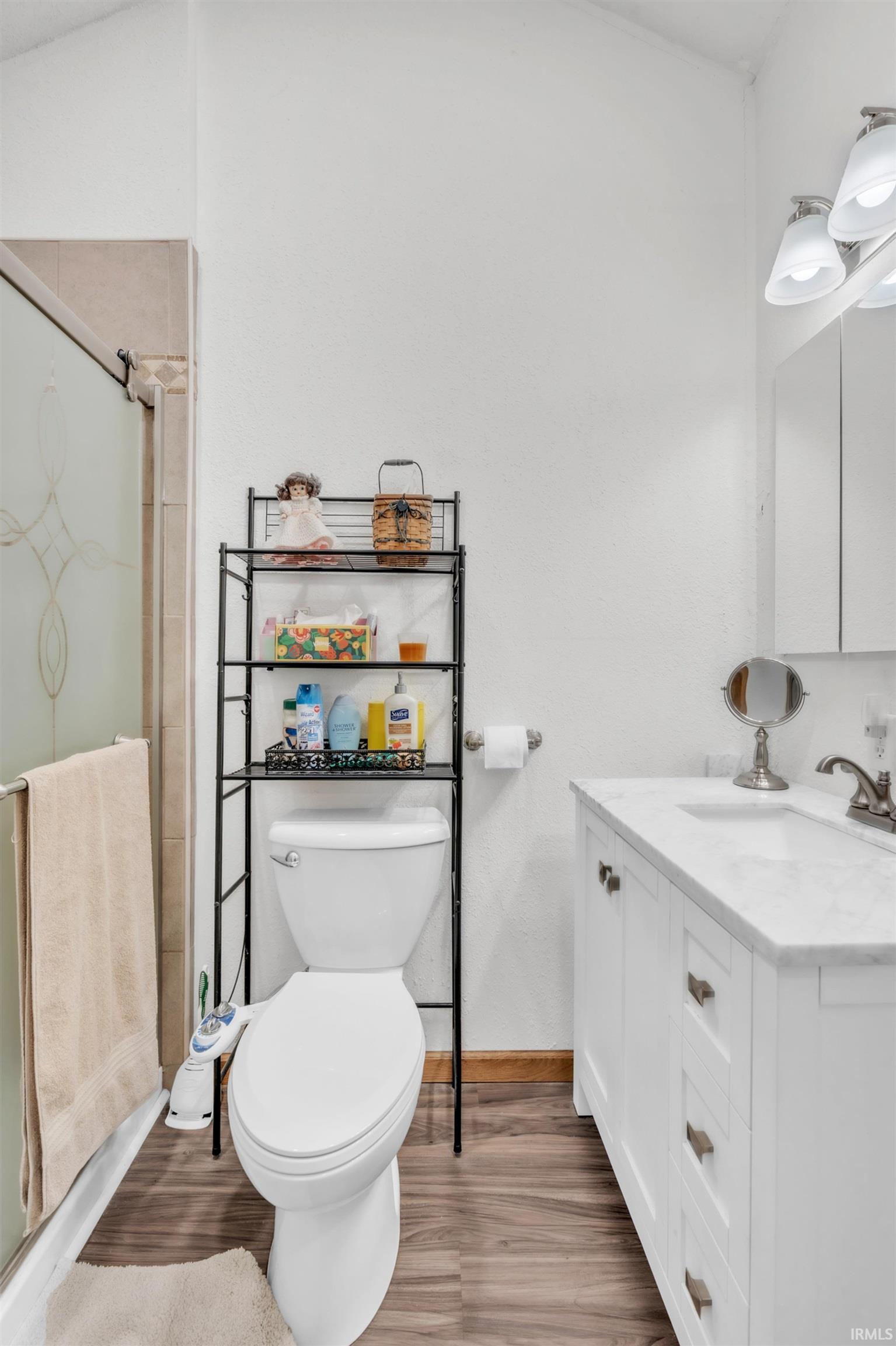 Bathroom featuring a white vanity with a marble-finish countertop, wood-finish flooring, and a glass-enclosed shower