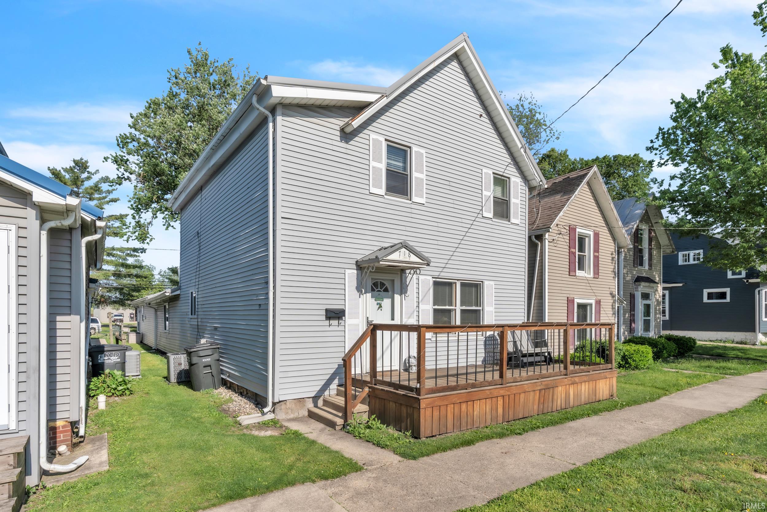 Two-story residence featuring light gray siding, a prominent front deck with wood railing, and white-trimmed windows with louvered shutters
