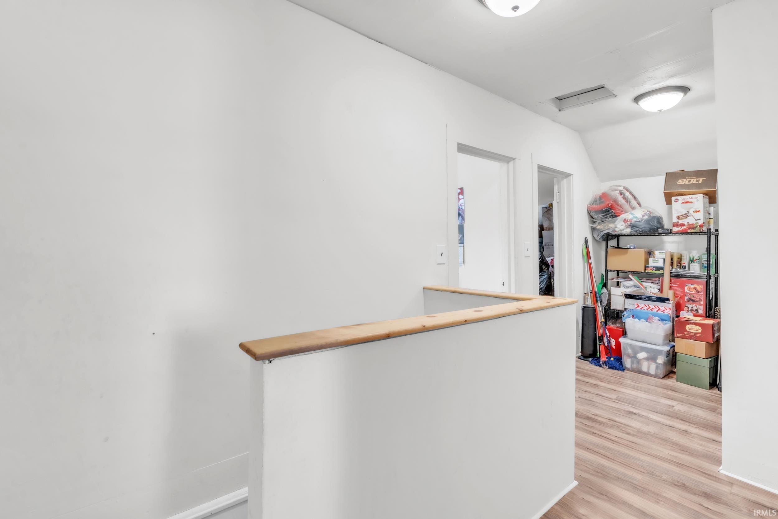 Upper-level hallway featuring wood-finish flooring, white walls, and a wood-capped half-wall