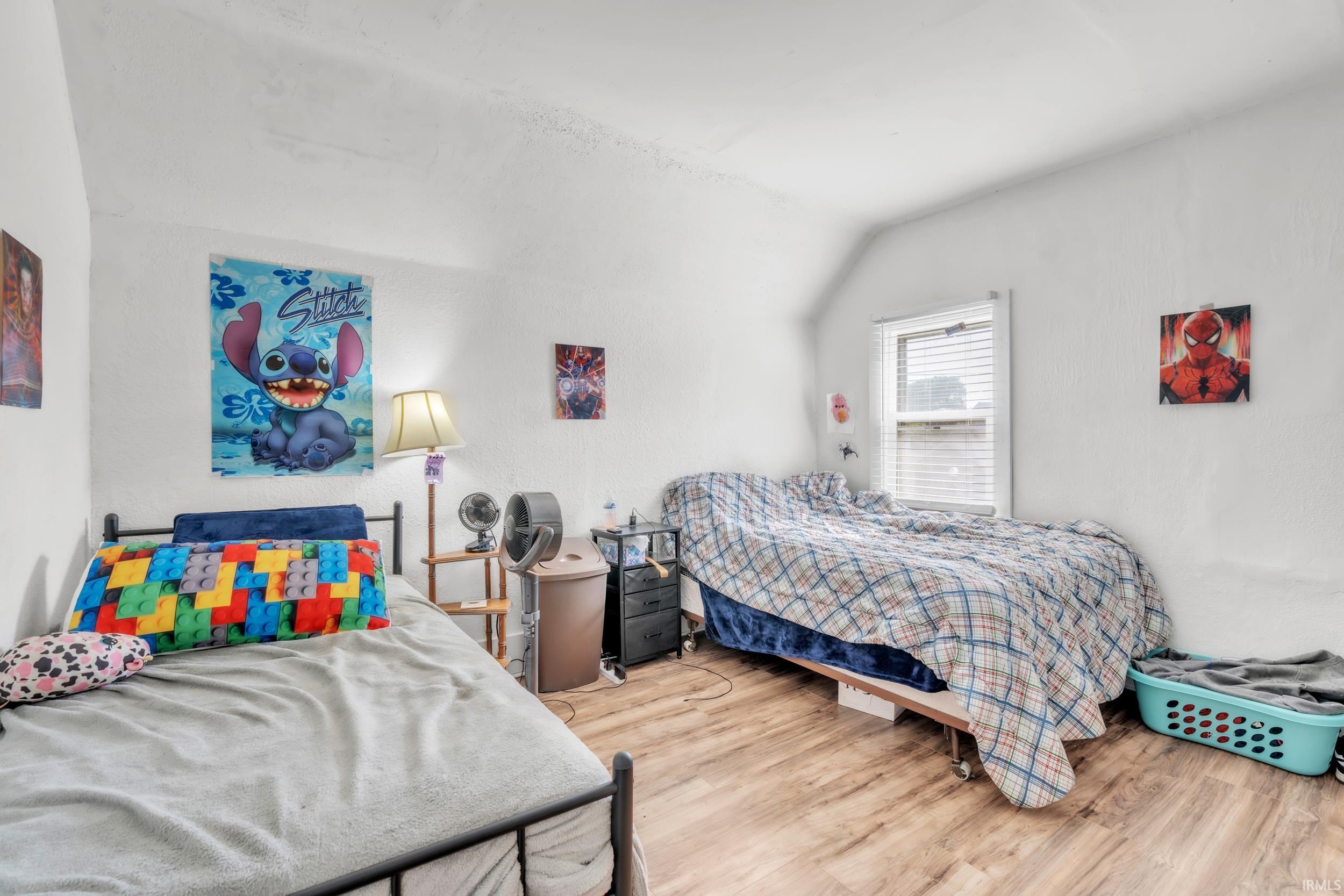 Interior room with white walls, wood-finish flooring, and a window featuring horizontal blinds