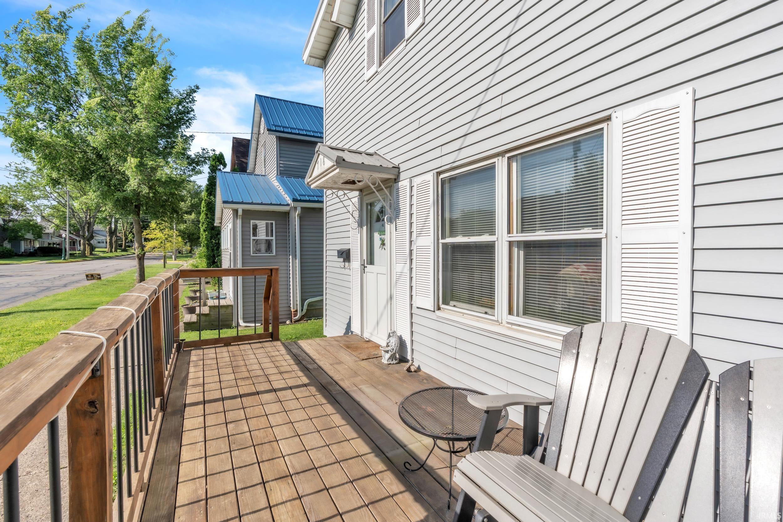 Inviting front porch featuring a wooden deck, dark wood railing with black metal spindles, and light-colored siding