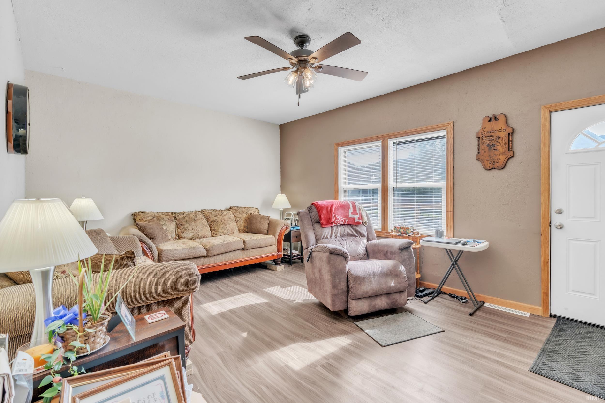 Living area featuring wood-finish flooring, a ceiling fan with integrated lighting, and neutral wall tones