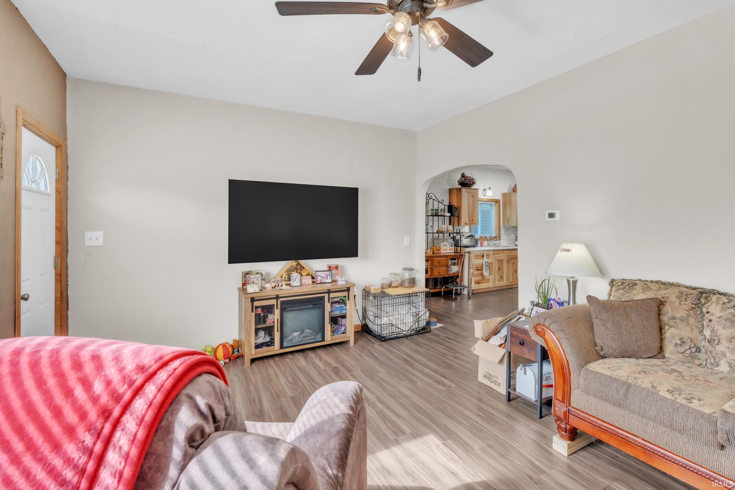 Living space featuring wood-finish flooring, a ceiling fan with integrated lighting, and an arched doorway leading to another room