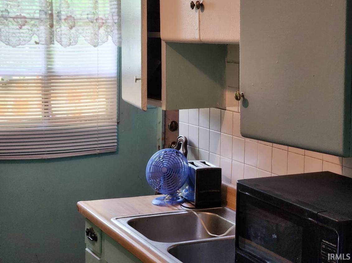 Kitchen area featuring a double basin stainless steel sink, wood-finish countertop, white square tile backsplash, and light-colored upper cabinetry
