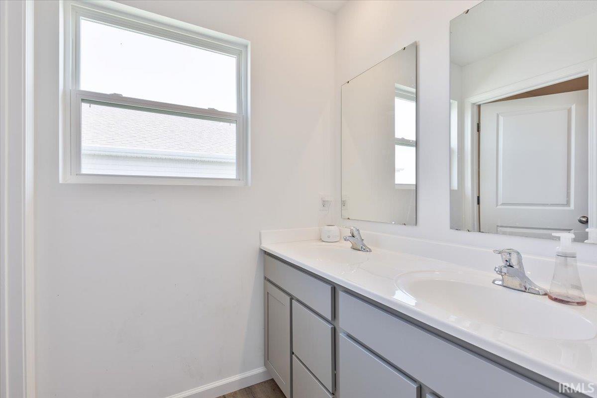 Double vanity featuring light gray cabinetry, integrated sinks, chrome faucets, and a broad wall mirror