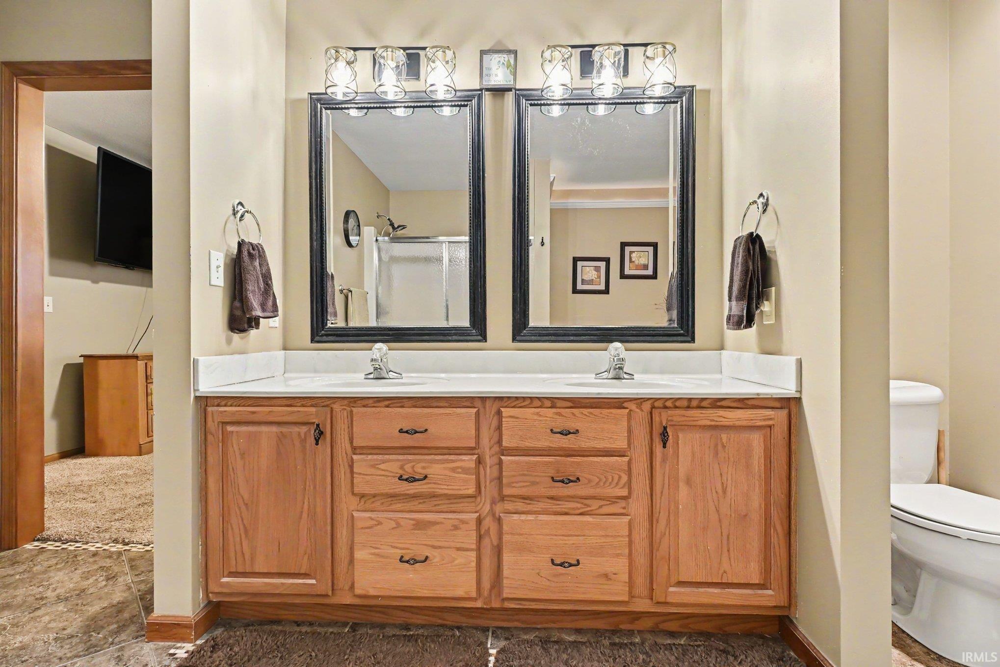Bathroom vanity featuring dual sinks, twin framed mirrors, and overhead light fixtures