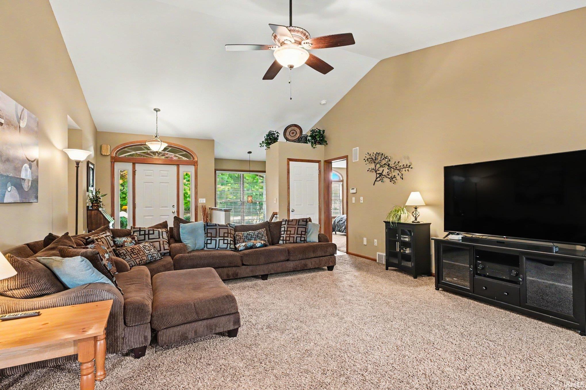 Spacious living area featuring vaulted ceilings, neutral carpeting, and a ceiling fan with light fixture