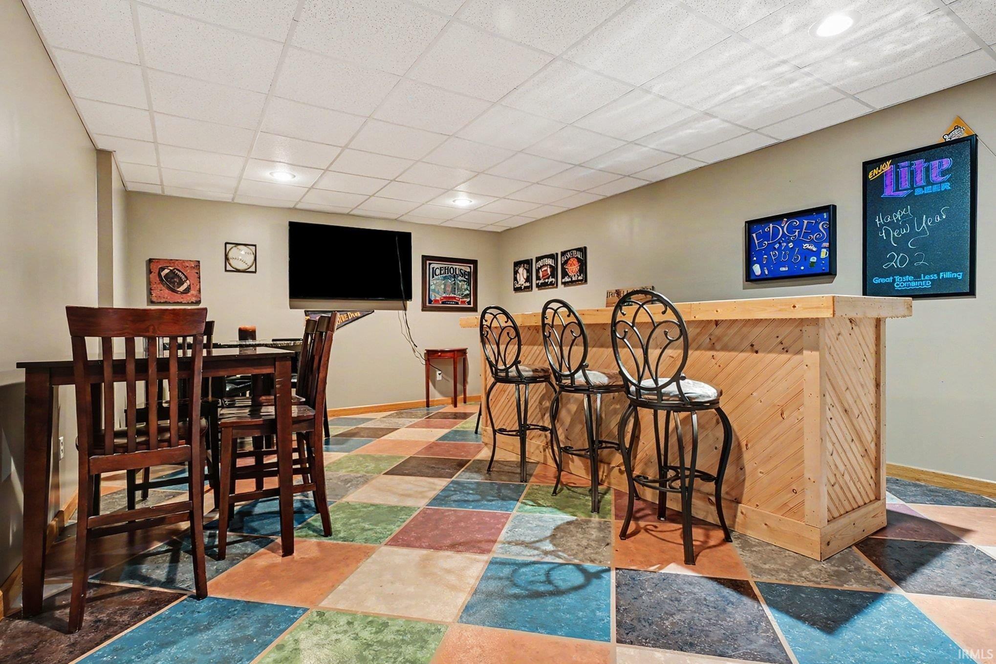 Entertainment space featuring a custom wood bar with diagonal paneling, multicolor square tile flooring, recessed ceiling lighting, and a drop ceiling
