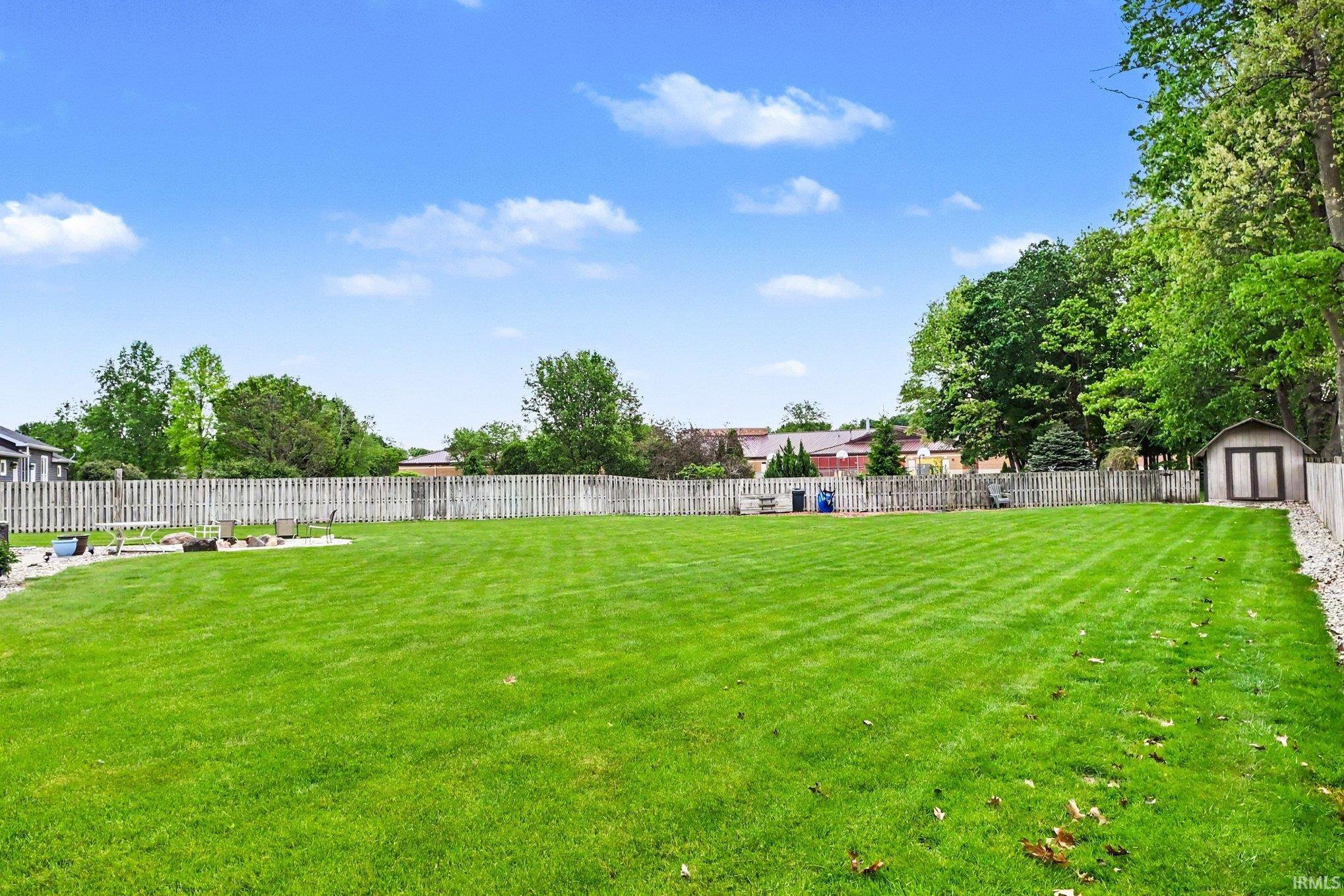 Expansive backyard featuring a manicured lawn, a wood fence perimeter, mature trees, and a detached storage shed with double doors