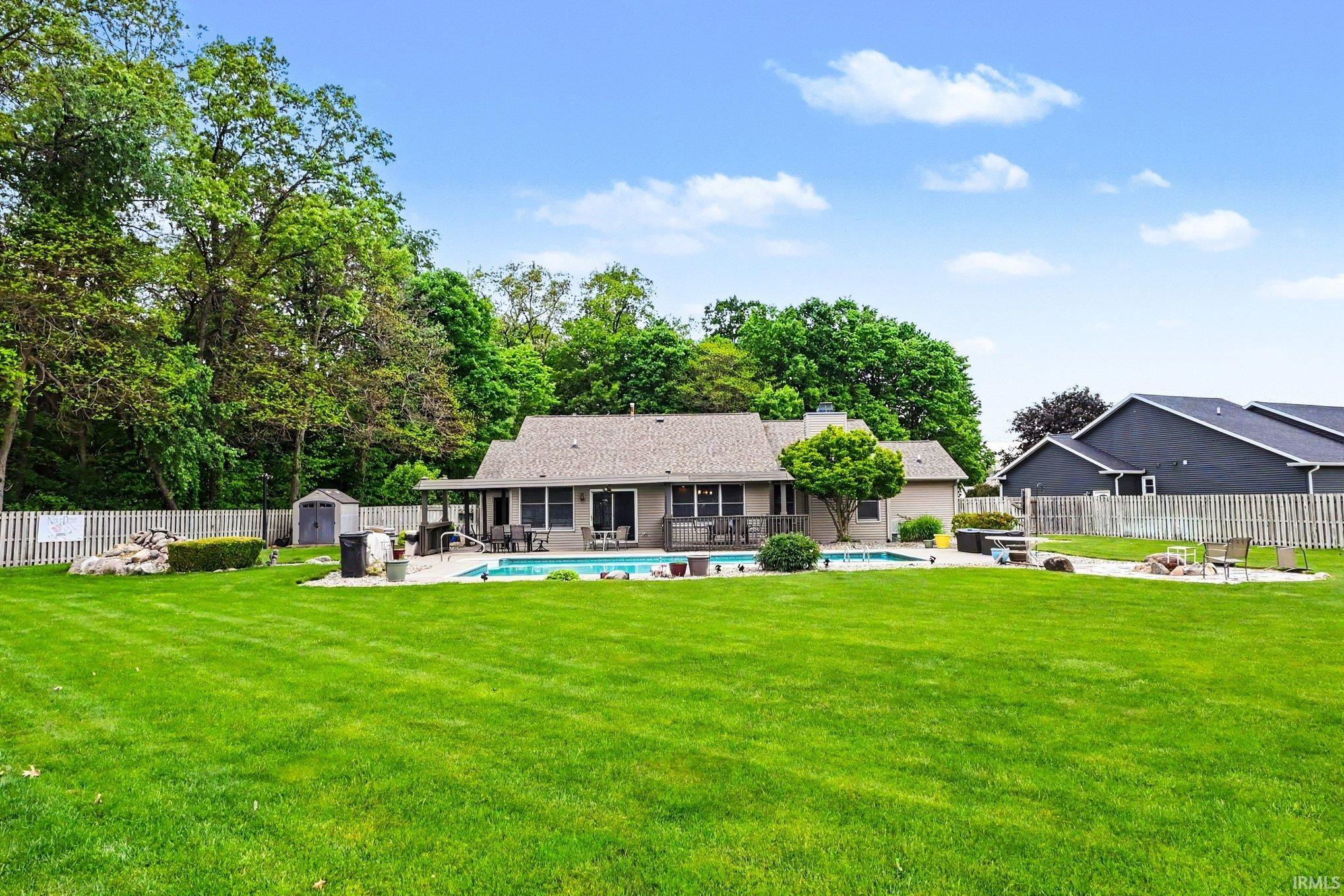 Expansive backyard featuring a manicured lawn, a swimming pool with a surrounding paved deck, and a covered patio area