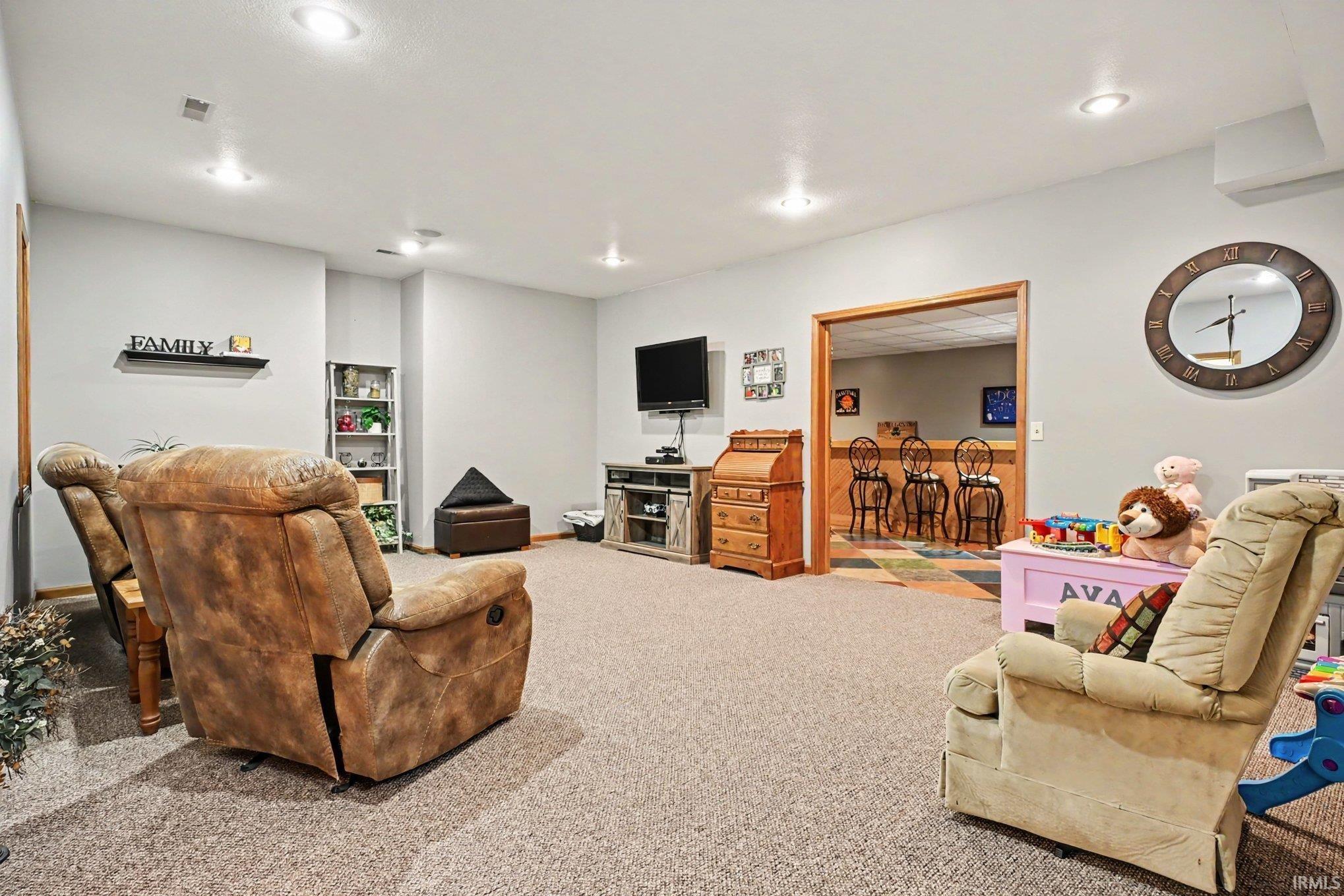 Carpeted room with recessed lighting and a wood-trimmed doorway opening to an additional room