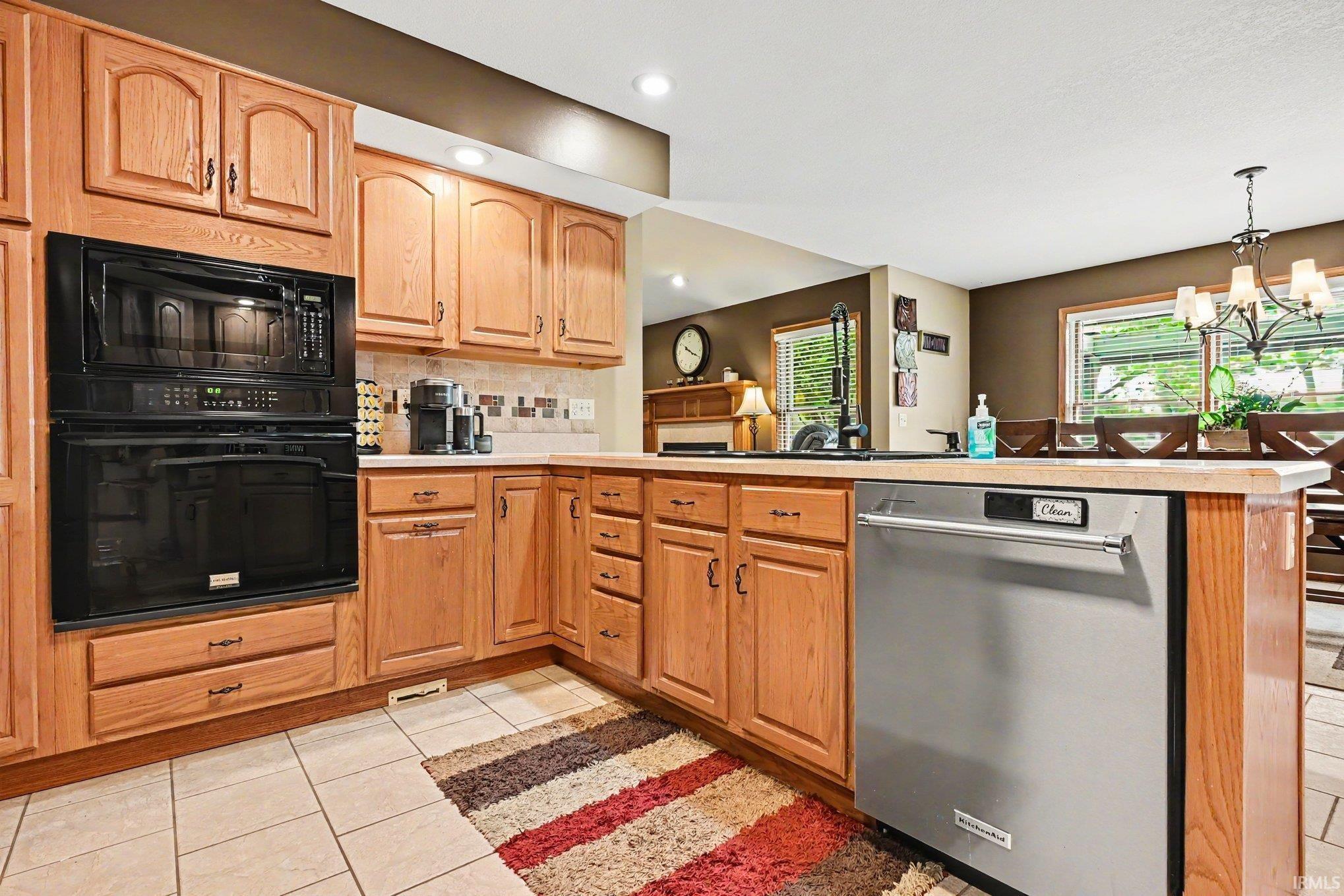 Kitchen featuring wood cabinetry, integrated black wall oven and microwave, stainless steel dishwasher, and tiled flooring
