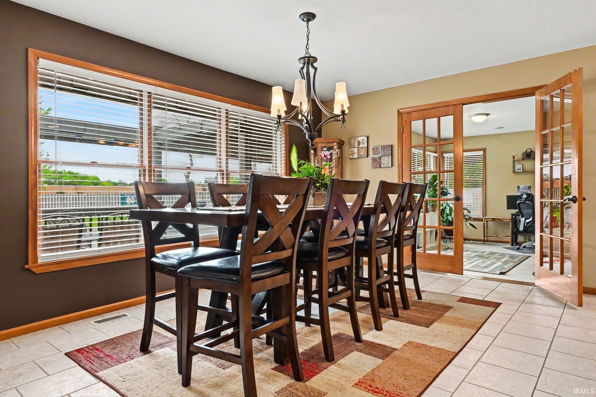 Dining area featuring neutral tile flooring, a multi-pane window with wood-finish trim, and a decorative chandelier