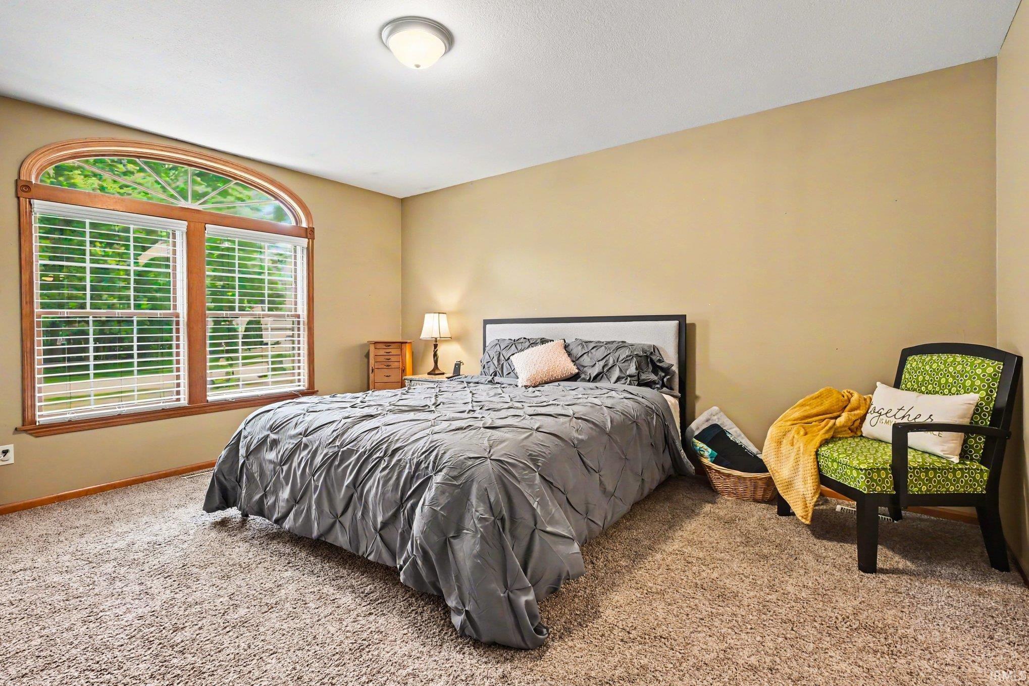 Bedroom featuring a large arched window with wood trim, neutral wall paint, and textured carpeting